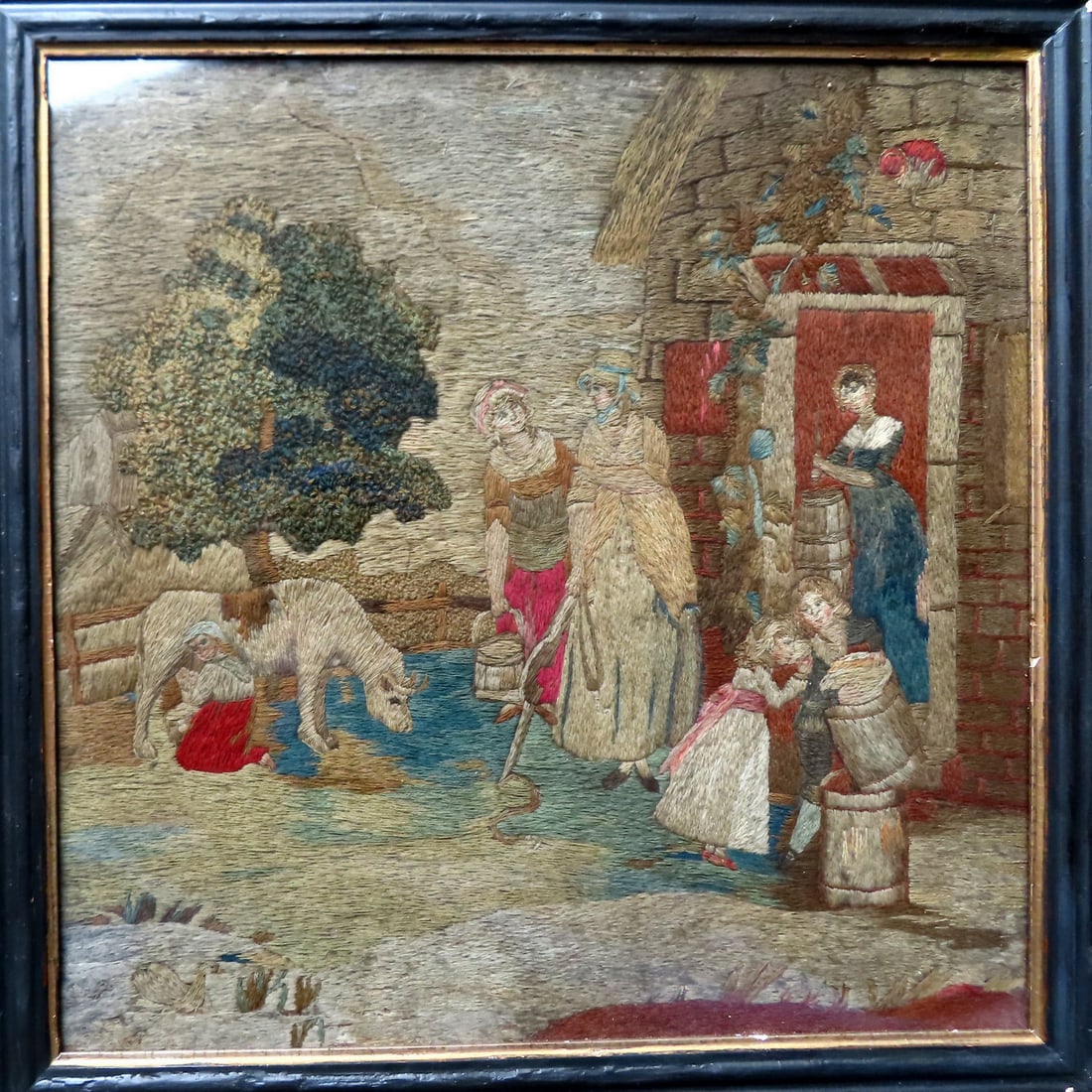 A silk embroidery farm scene depicting a young lady milking a cow and others either carrying milk in: A silk embroidery farm scene depicting a young lady milking a cow and others either carrying milk in buckets or churning butter, late 18th century and in very good original condition. The frame has so