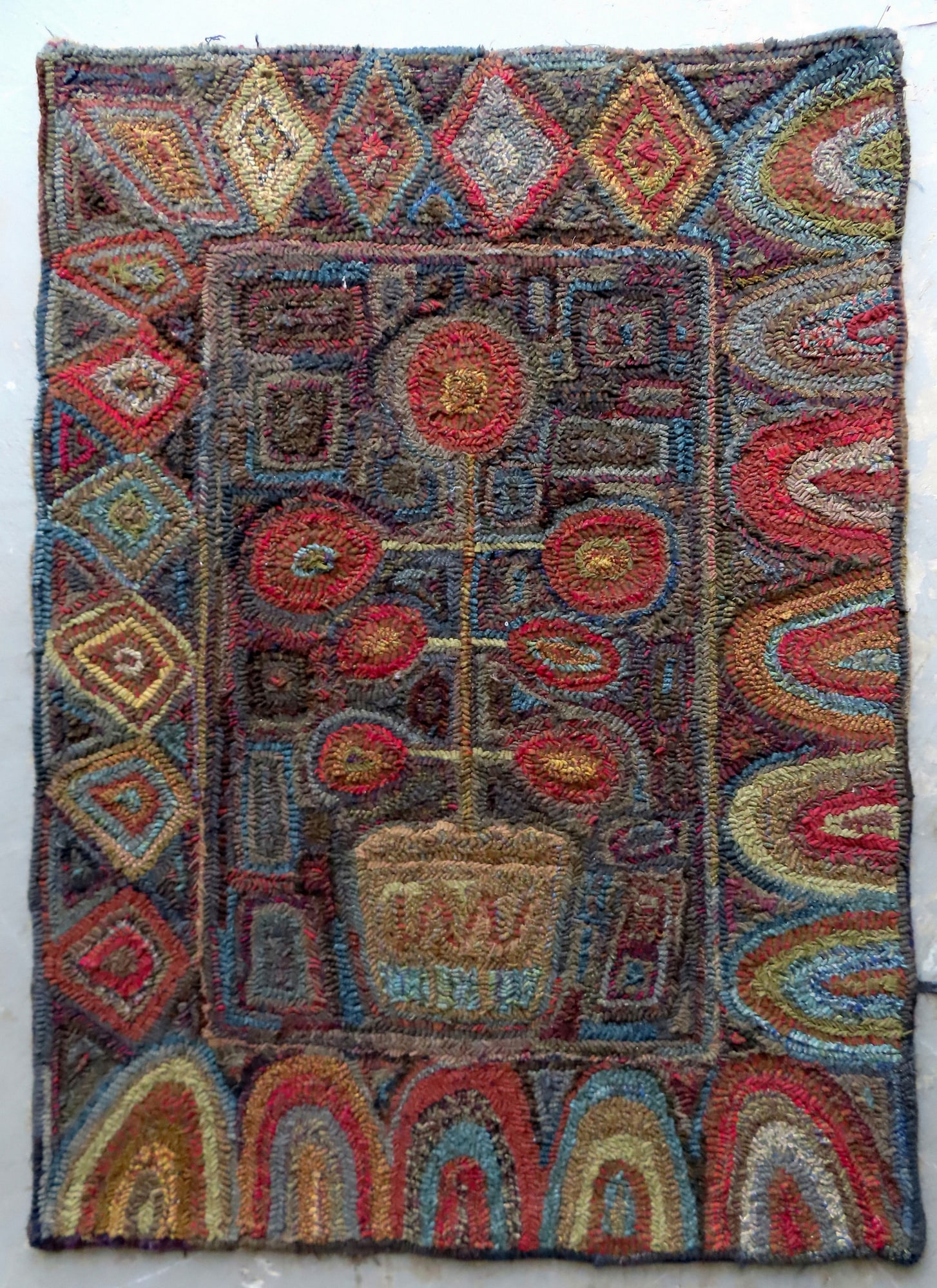 A folk art design hooked rug decorated with a central image of a stylized flower pot with flowers (1 of 4)