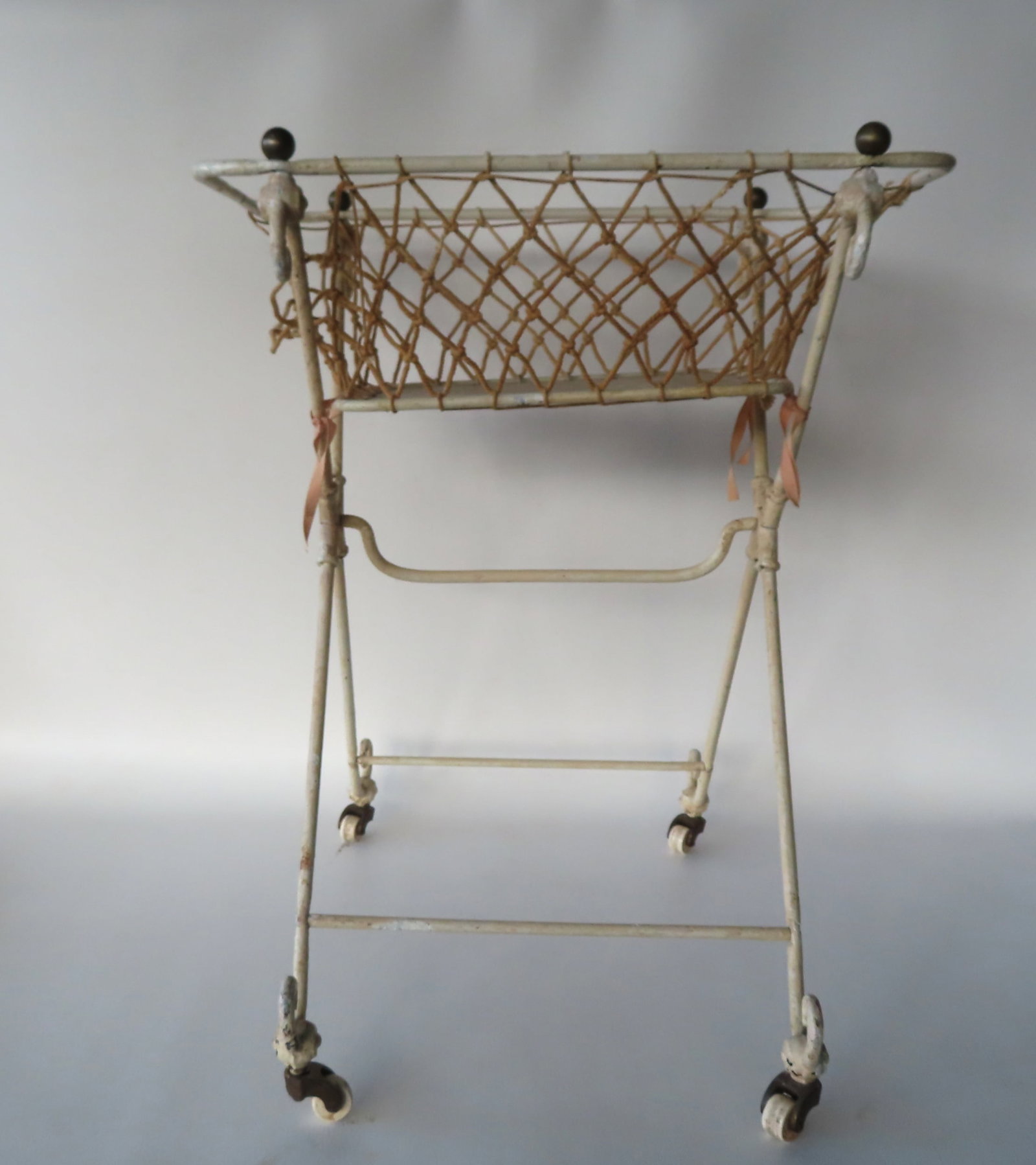 A Victorian era iron basket on porcelain wheels, circa 1880 - one end of the string netting is loose: A Victorian era iron basket on porcelain wheels, circa 1880 - one end of the string netting is loose from the frame, otherwise very good condition. Measures 21 1/2"W x 15"D x 26 1/2"H. Provenance: Fro