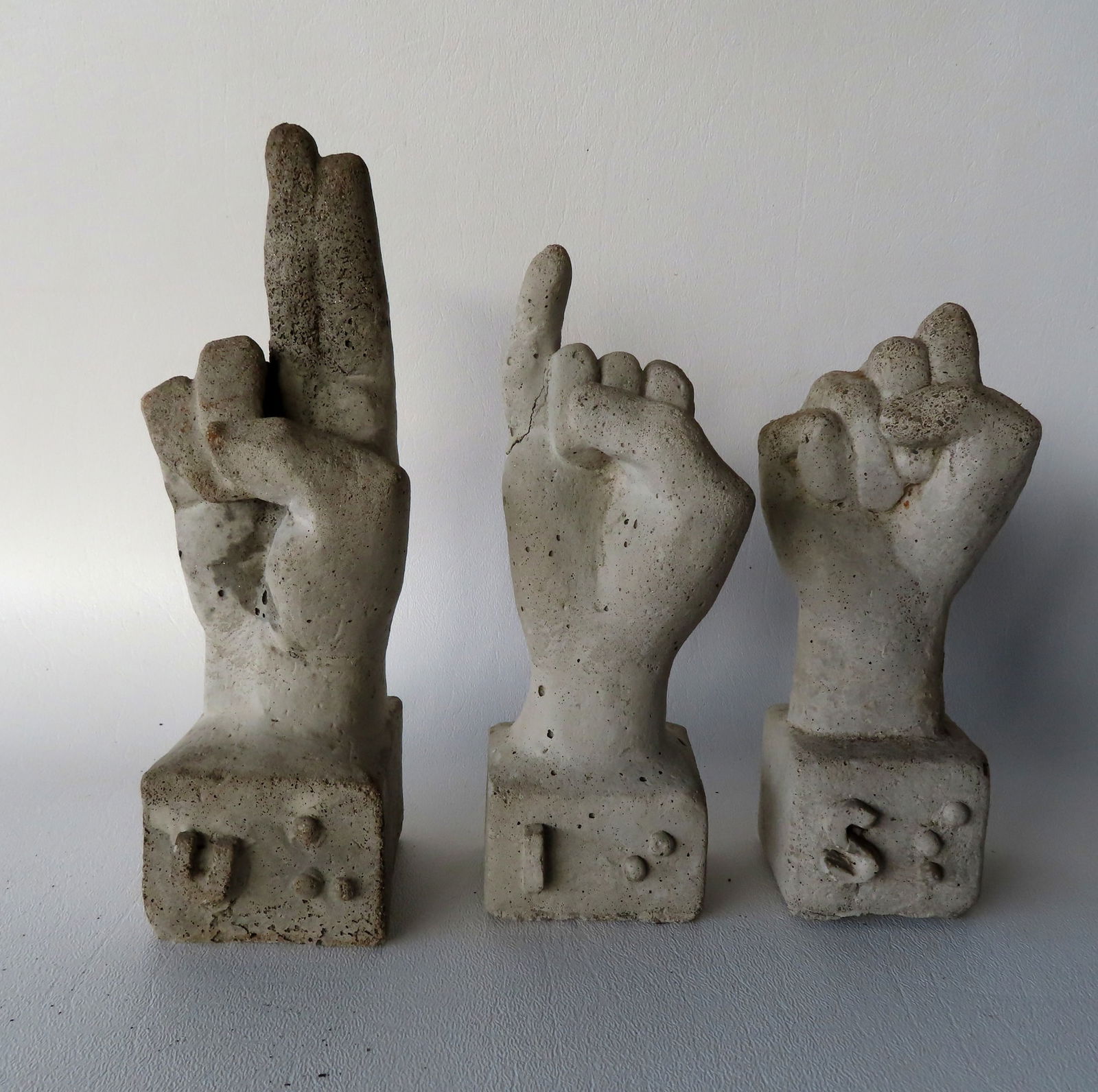 Three concrete sign language hands and figures with brail symbols on base for the letters S, U and (1 of 3)