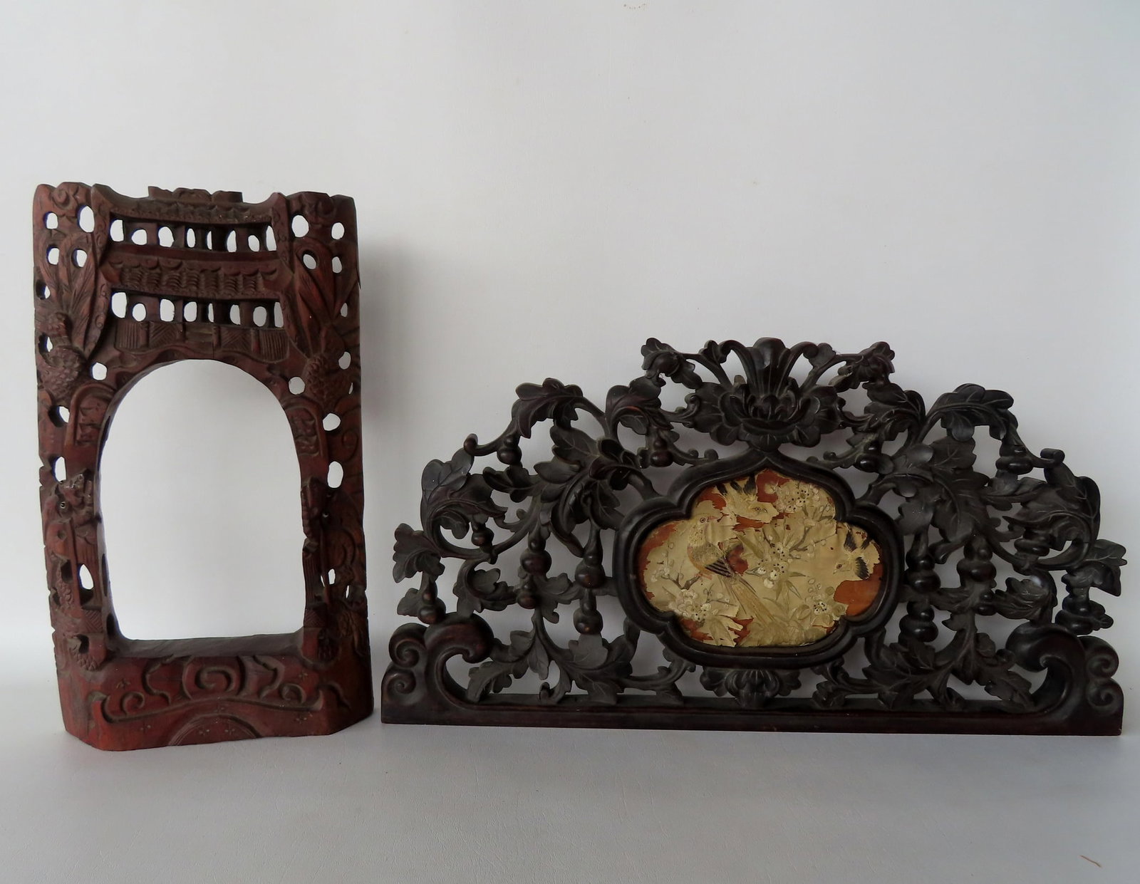 Two carved wooden oriental ornaments, 19th century. The largest in teakwood with open work carving: Two carved wooden oriental ornaments, 19th century. The largest in teakwood with open work carving of leaves and berries surrounding the central medallion housing a silk embroidery of exotic bird - ex