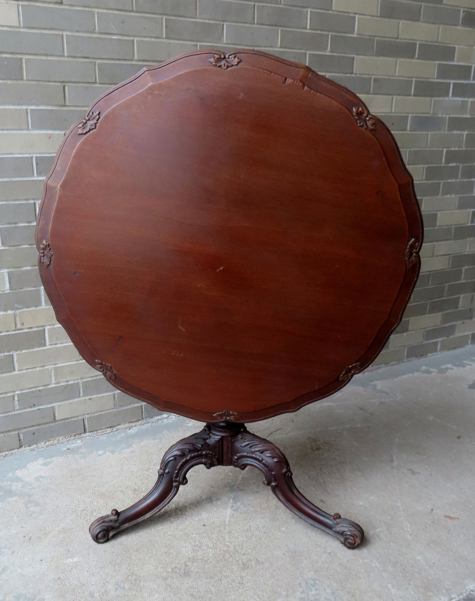 An elaborately carved mahogany tea table having a shaped top with carved perimeter over a carved (1 of 8)