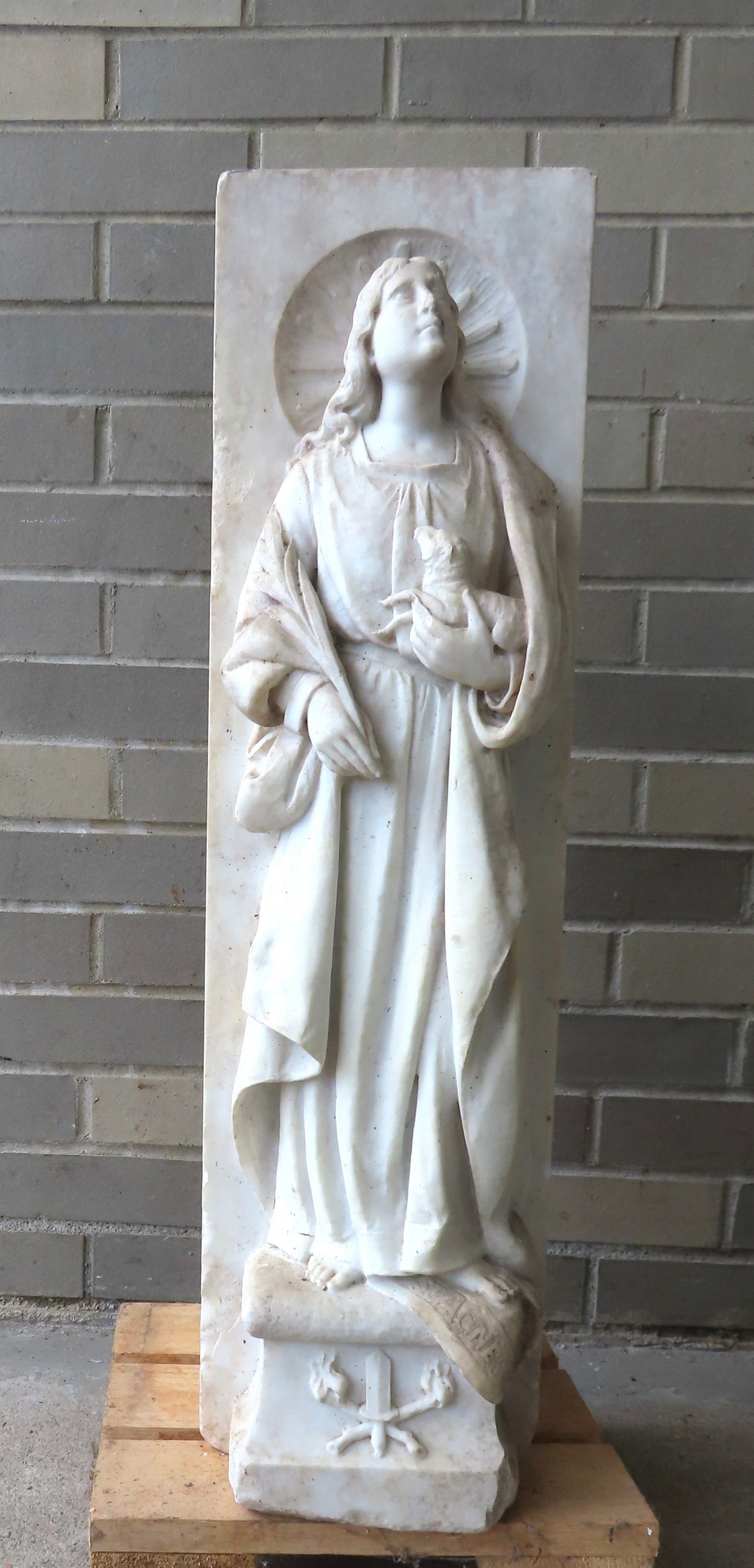 An early relief carved marble sculpture of St. Agnes of Rome holding a lamb (signed "St. Agnes": An early relief carved marble sculpture of St. Agnes of Rome holding a lamb (signed "St. Agnes" above base). The half body sculpture is carved into the front section of a square column, probably part 