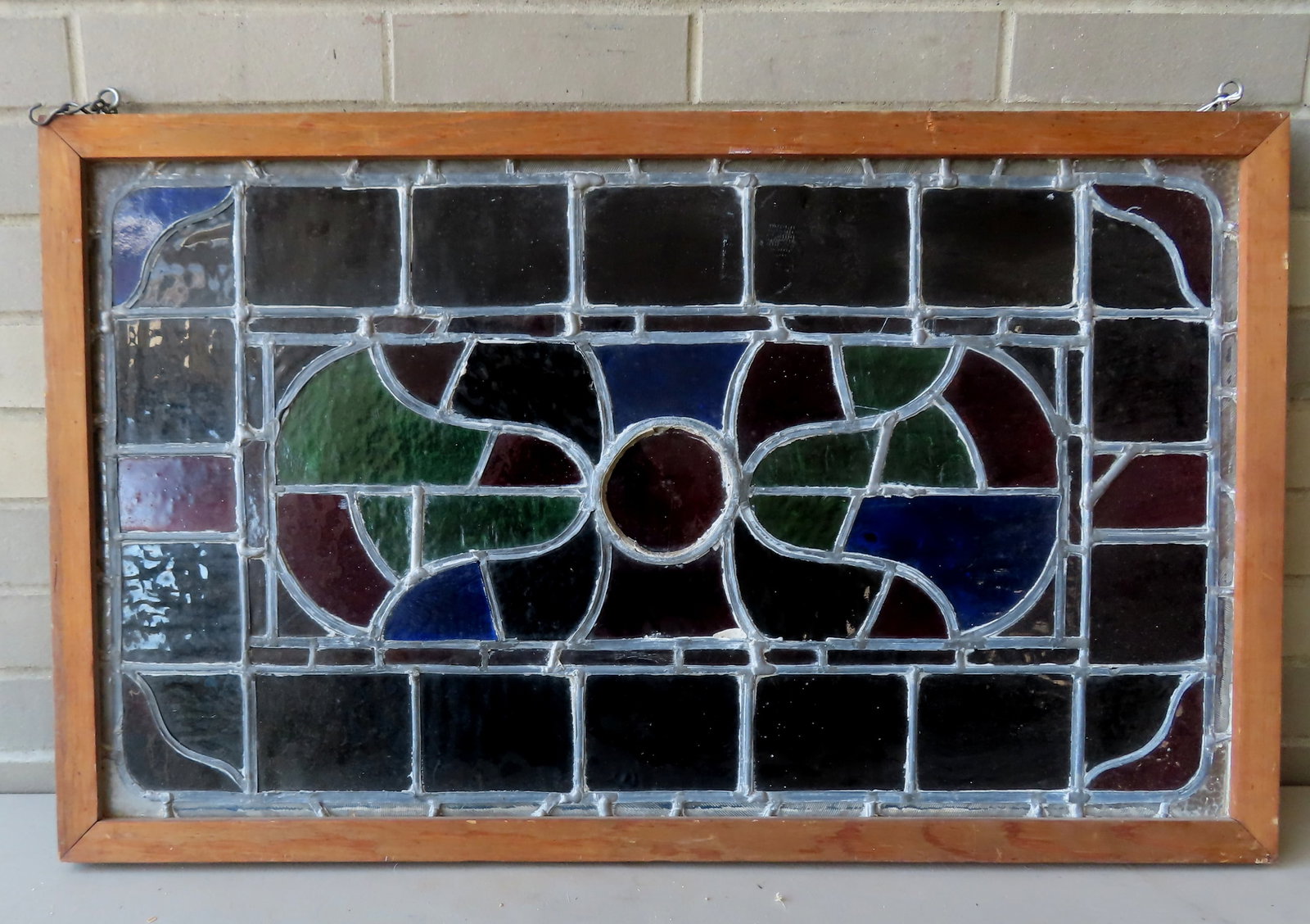 A stained in leaded glass window with a bullseye panel flanked by bells on each side and having: A stained in leaded glass window with a bullseye panel flanked by bells on each side and having rectangular glass panels around border, circa 1920 with newer wooden frame. Very good condition. Measure