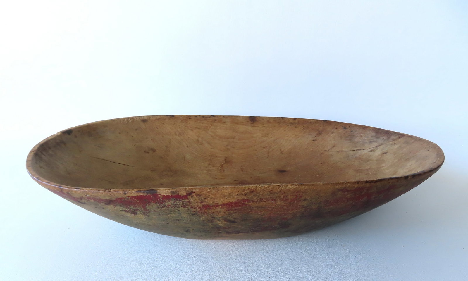 A small primitive oval treenware bowl, traces of original red paint. Two small hairlines extending: A small primitive oval treenware bowl, traces of original red paint. Two small hairlines extending from rim, otherwise very good original condition with expected use wear - 21"L x 10"W x 4"H.