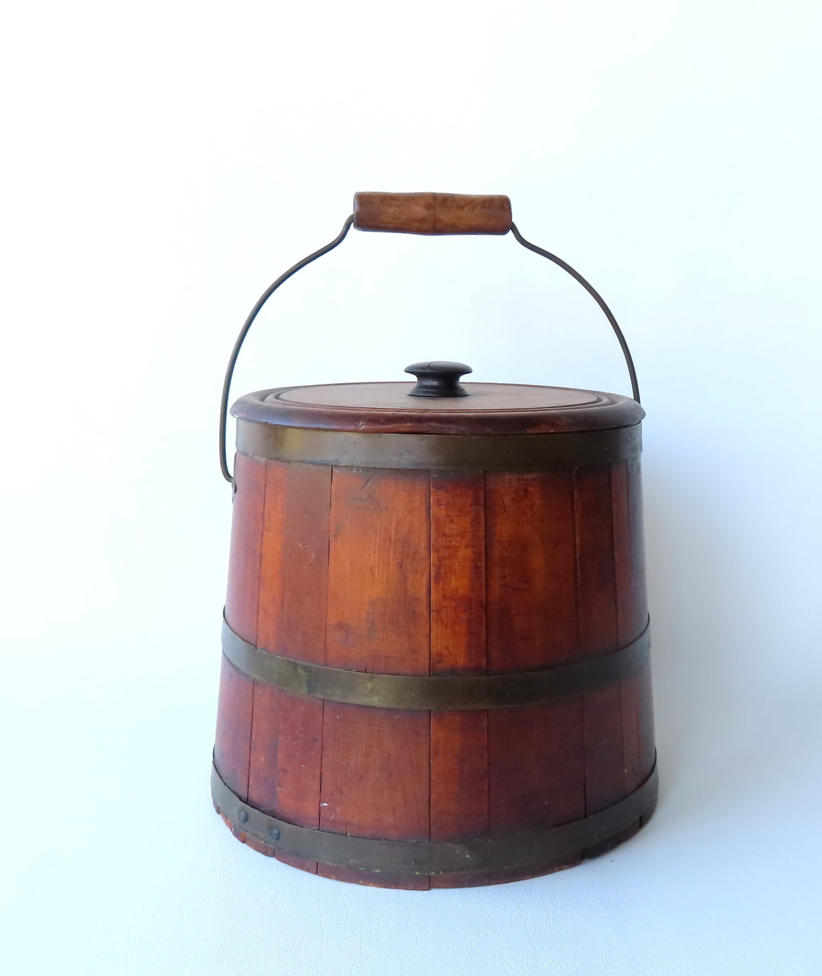 A lidded staved bucket with bail handle with riveted metal bands and diamond shape metal side: A lidded staved bucket with bail handle with riveted metal bands and diamond shape metal side mounts, typically found on Shaker buckets. 19th century. Measures 10 1/2"H x 10 3/4" diameter at base . Pr