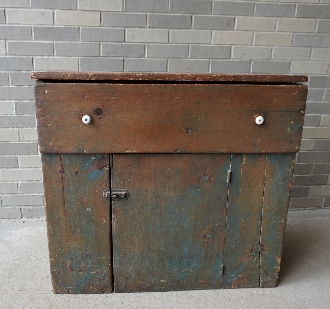 A small primitive floor cupboard having 1 large and deep drawer over 1 door, scraped down to: A small primitive floor cupboard having 1 large and deep drawer over 1 door, scraped down to original blue-green paint with worn top. Older porcelain pulls which may not be original (one pull missing 