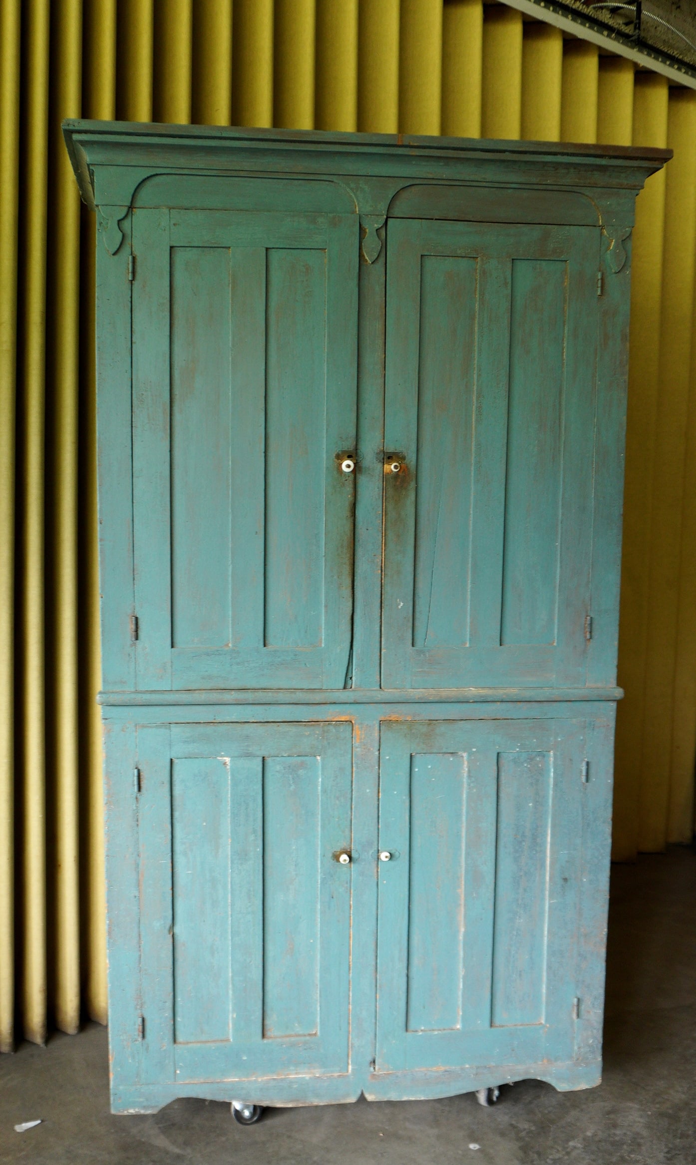 Large country 4 door cupboard scraped down to old turqoise colored paint - some overpaint: Large country 4 door cupboard have 2 paneled doors over 2 paneled doors mounted on cutout base, and scraped down to a turquoise colored paint with modern turquoise over paint, circa 1850. Condition: C