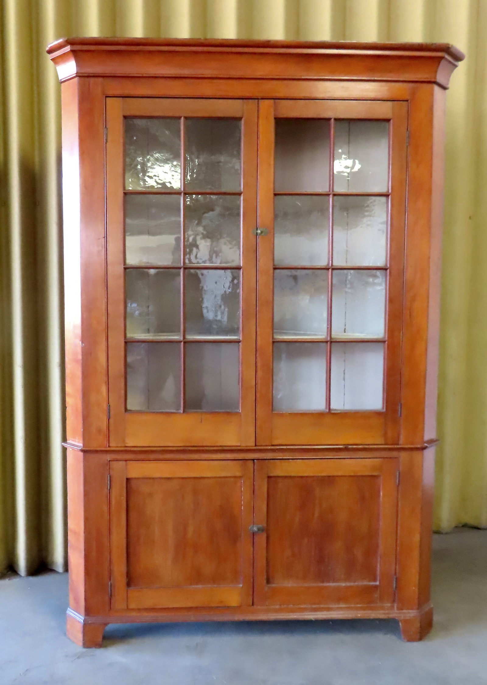 A very fine cherry one piece corner cupboard having 2 doors each with 8 glass panels (all original: A very fine cherry one piece corner cupboard having 2 doors each with 8 glass panels (all original wavy glass with the exception of 1 replaced glass), over 2 paneled doors and original grown molding, 