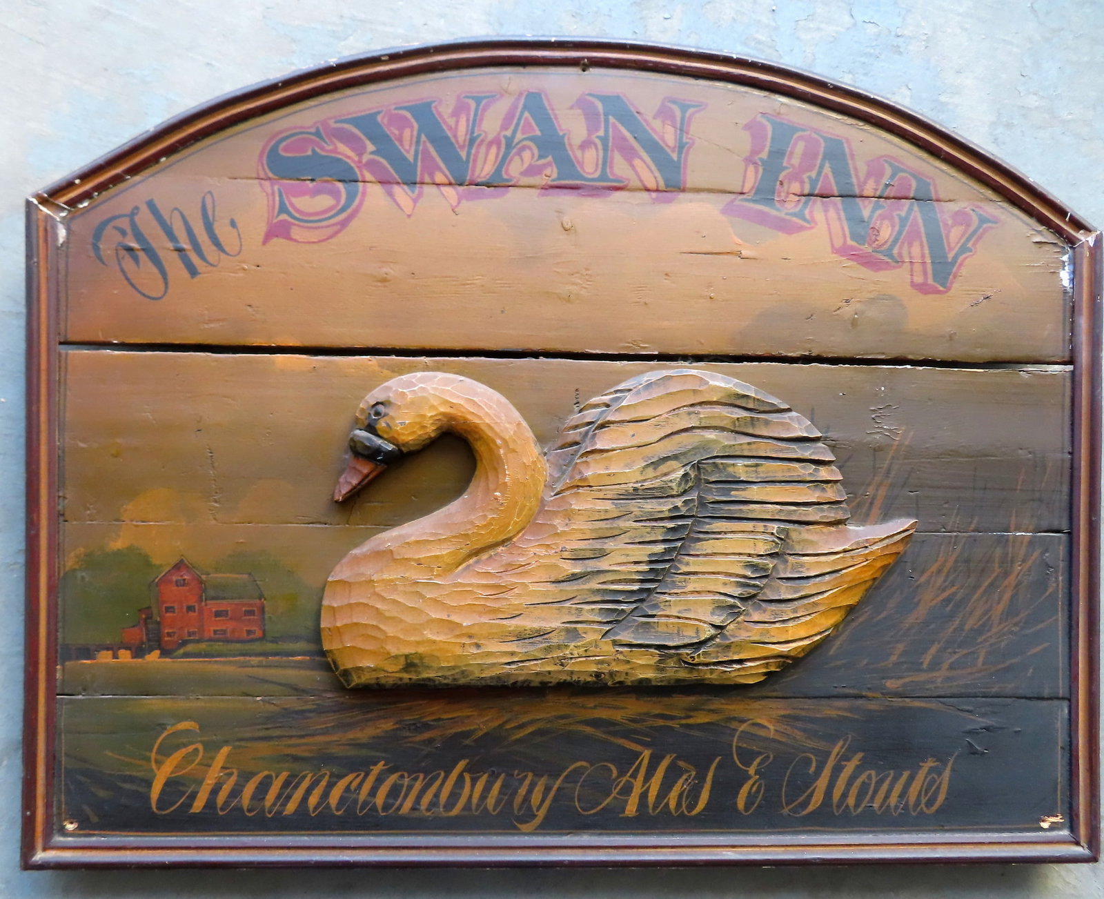An English wooden pub sign marked "THE SWAN INN / CHANCTONBURY / ALES & STOUTS", decorated with a: An English wooden pub sign marked "THE SWAN INN / CHANCTONBURY / ALES & STOUTS", decorated with a carved wooden swan in relief in the center of sign which is all hand painted in a landscape scene with