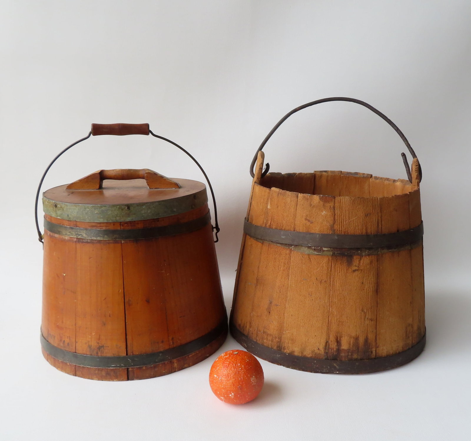 Two early buckets. The first a staved well bucket with iron bail handle attached to ears on each: Two early buckets. The first a staved well bucket with iron bail handle attached to ears on each side. The 2 iron straps held together with forged pins. The sides weathered as expected with water use,