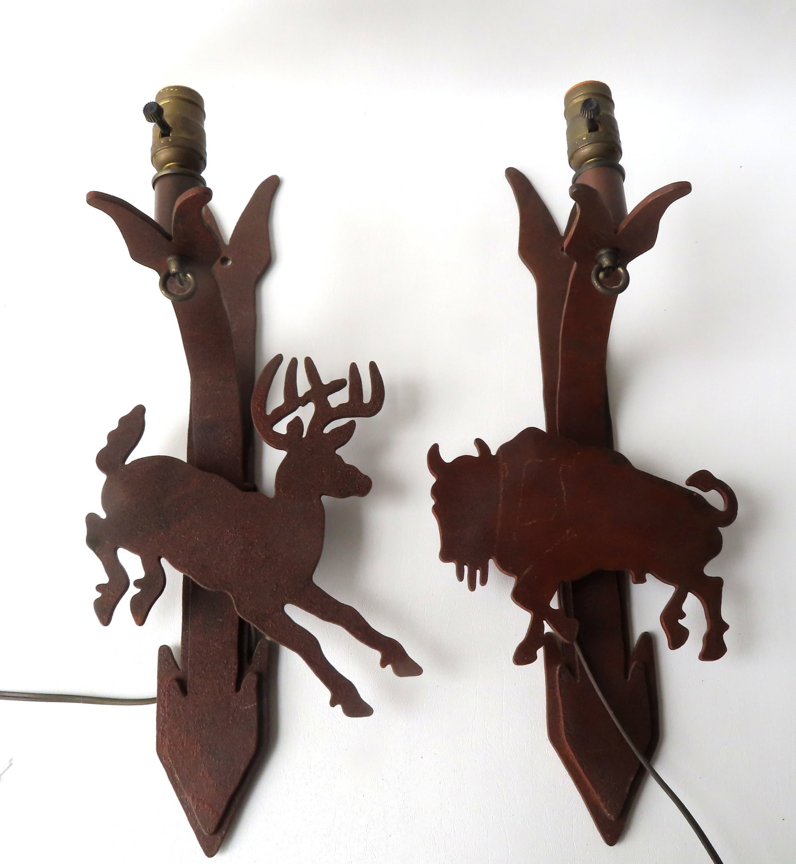 A pair of custom made rustic cast iron electric wall sconces with wild animals attached to arrow: A pair of custom made rustic cast iron electric wall sconces with wild animals attached to arrow shaped wall mounting. One in the form of a running deer and the other a buffalo, circa 1950-70. Both in