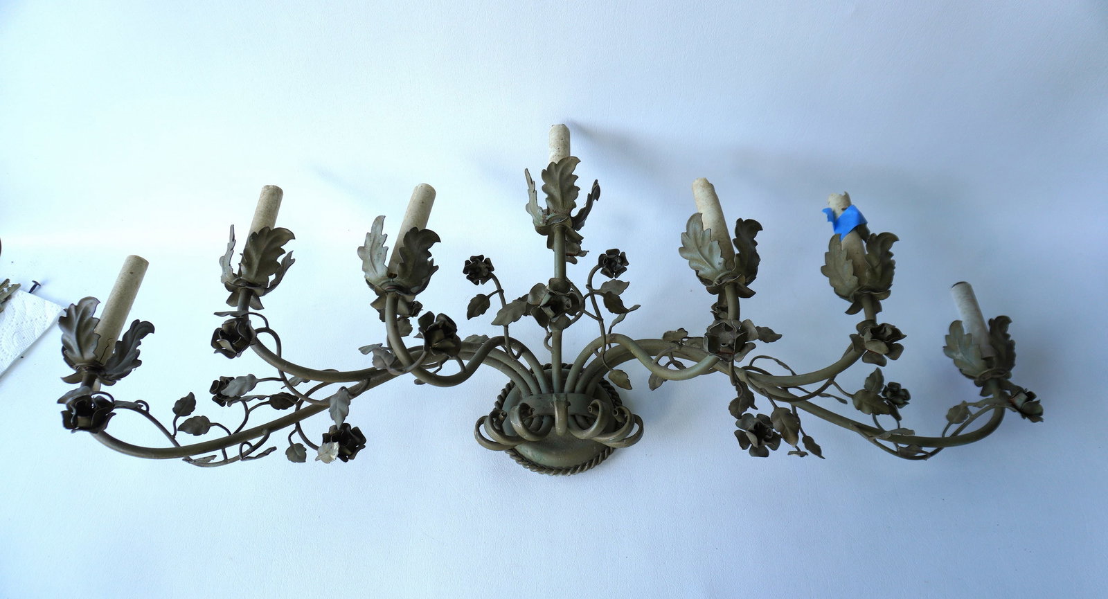 A wall mount painted tin candelabra (electric) with 7 lights and decorated with flowers on vines,: A wall mount painted tin candelabra (electric) with 7 lights and decorated with flowers on vines, circa 1940. Several of the white candleholders that surround the electrical fixture holding the light 