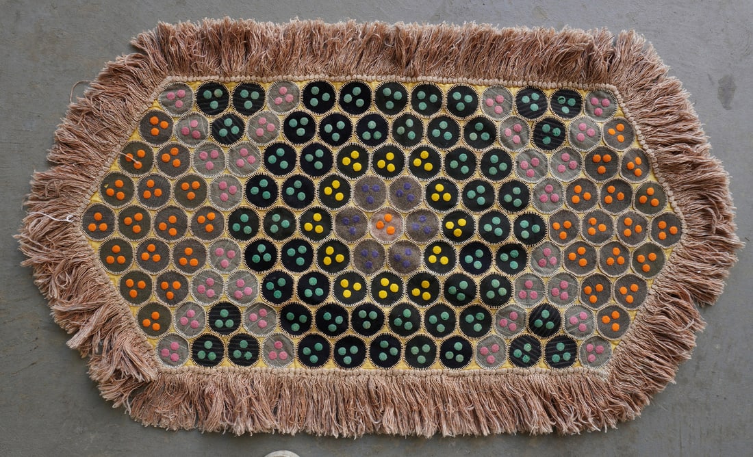 A folk art table penny rug with long fringe around border, 19th century. Some staining and losses to: A folk art table penny rug with long fringe around border, 19th century. Some staining and losses to the bed ticking backing, else very good condition. Measures 52"L x 30"W.