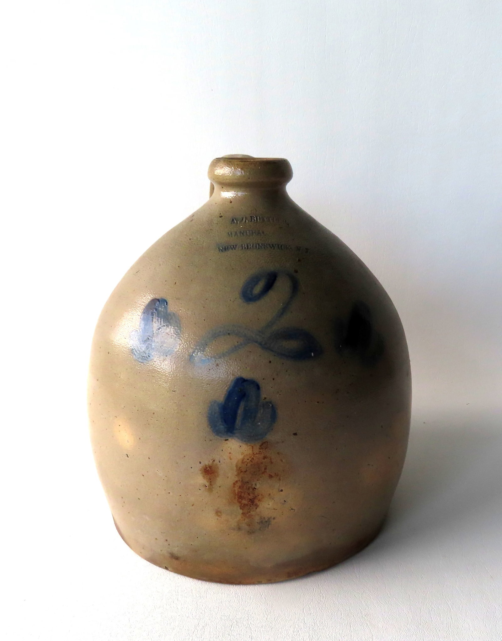 Marked "A.J. BUTLER / MANUFACTURER / NEW-BRUNSWICK NJ" stoneware 2 gallon jug decorated with 3 small: Marked "A.J. BUTLER / MANUFACTURER / NEW-BRUNSWICK NJ" stoneware 2 gallon jug decorated with 3 small cobalt blue flowers surrounding a script "2". Some staining and small drilled hold an back side of 