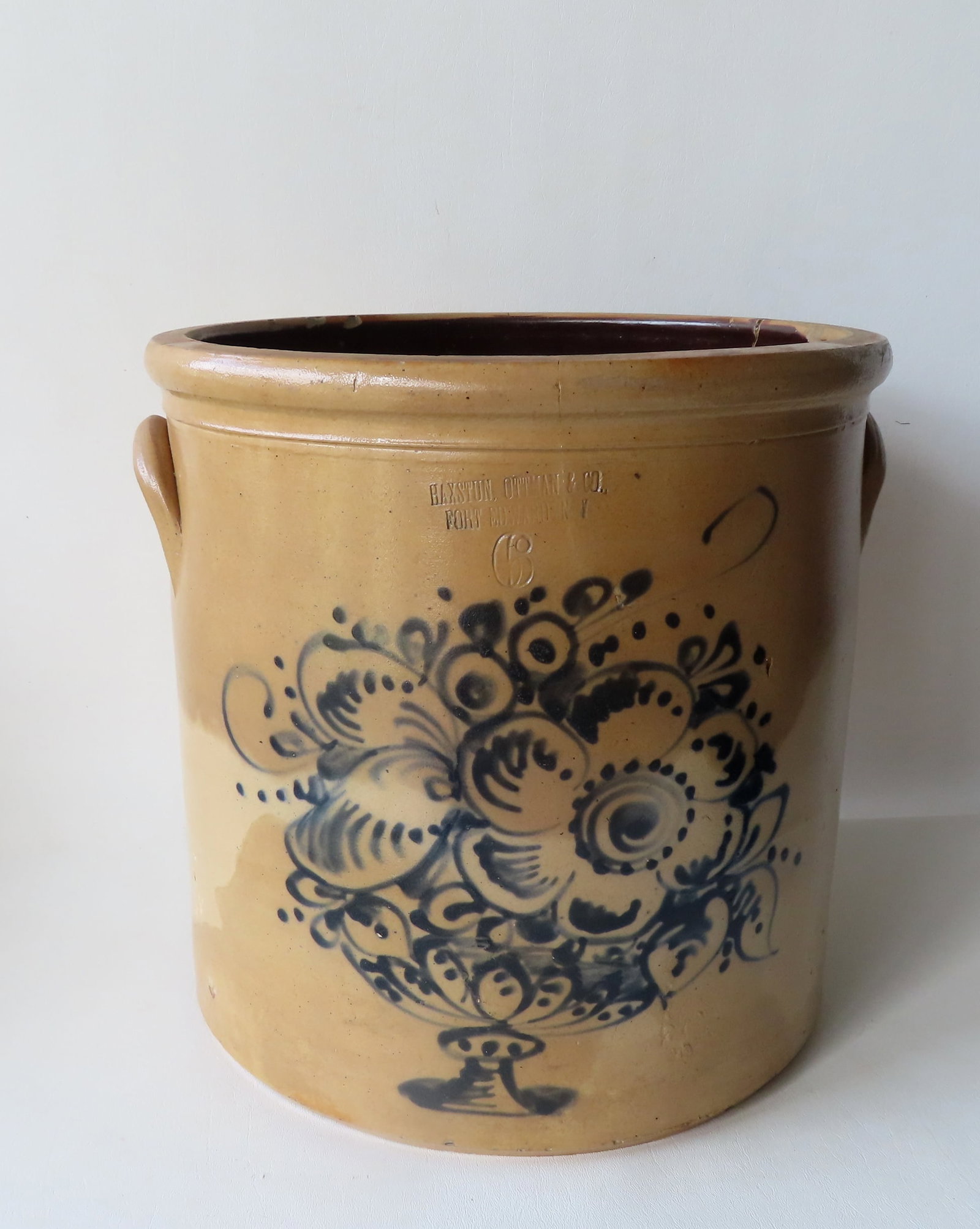 Marked "HAXSTUN OTTMAN & CO. / FORT EDWARD N.Y.", large stoneware 6 gallon crock decorated with a: Marked "HAXSTUN OTTMAN & CO. / FORT EDWARD N.Y.", large stoneware 6 gallon crock decorated with a cobalt blue flowers within an urn shaped vase - 14"W x 13 1/2"H. Staining, 2 interior rim chips, 2 hai