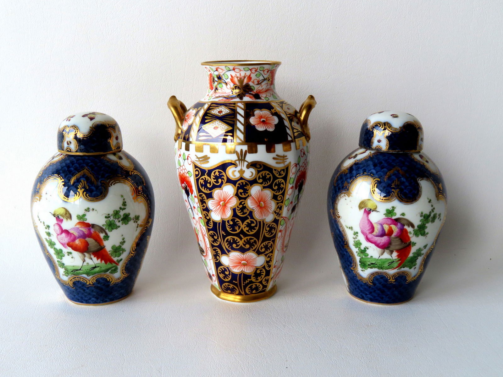 Two early Worcester tea caddies and a Royal Crown Derby double handle vase. The matching tea: Two early Worcester tea caddies and a Royal Crown Derby double handle vase. The matching tea caddies, with 18th century hallmarks, are decorated with hand painted exotic birds and butterflies with gol
