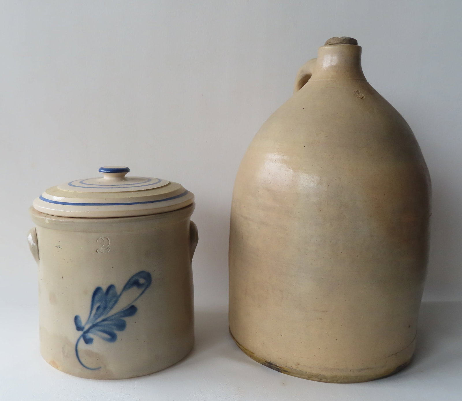 Two pieces of stoneware. The first a 2 gallon crock decorated with a cobalt blue leaf - tiny flake: Two pieces of stoneware. The first a 2 gallon crock decorated with a cobalt blue leaf - tiny flake on interior edge of rim and a chip out of one of the ears, else good condition - 10 diameter x 9 1/8"