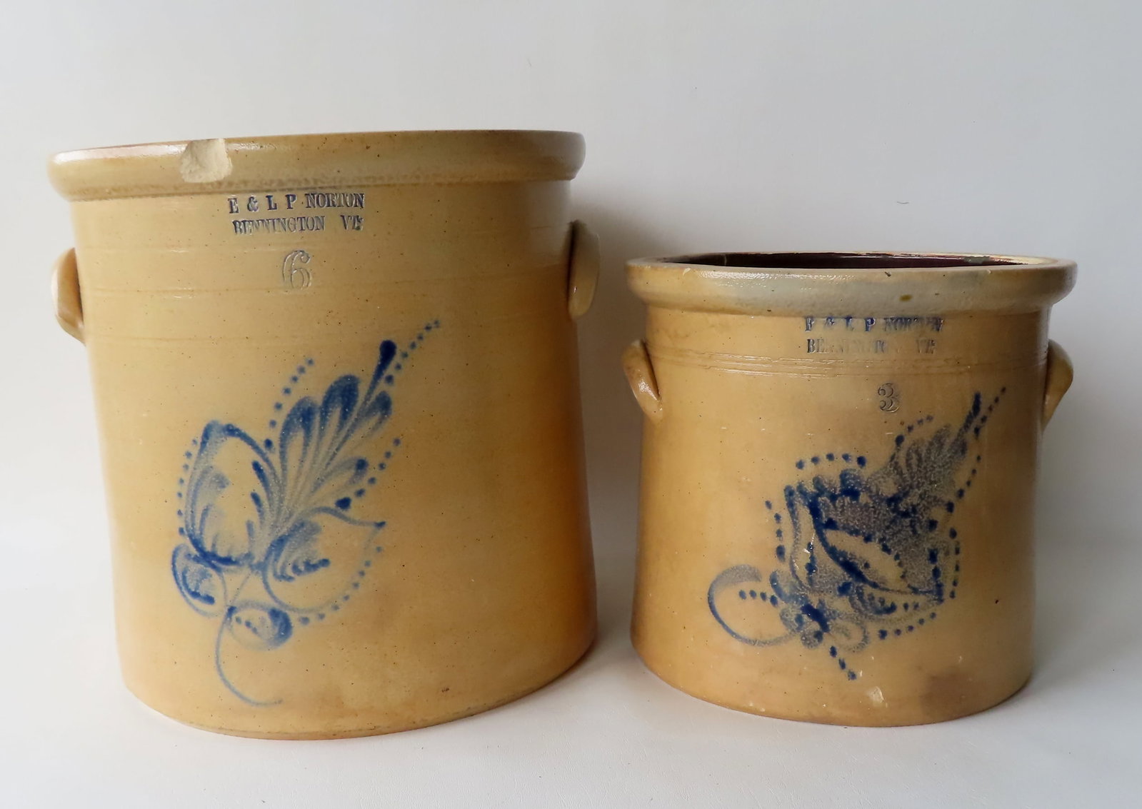 Two stoneware crocks stamped ""E & LP NORTON / BENNINGTON VT". The first, 5 gallon, decorated with a: Two stoneware crocks stamped ""E & LP NORTON / BENNINGTON VT". The first, 5 gallon, decorated with a cobalt blue flower - sizable chip on front edge of rolled rim, smaller chip on backside of rolled r