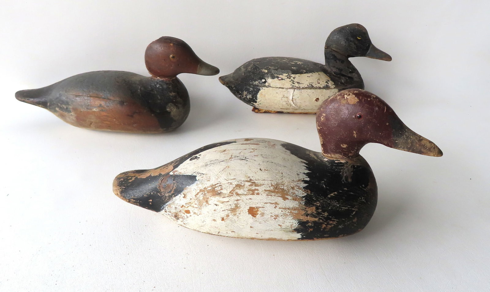 Grouping of 3 primitive decoys, late 19th to early 20th century. Includes: Canvasback with glass: Grouping of 3 primitive decoys, late 19th to early 20th century. Includes: Canvasback with glass eyes in original paint, and 2 Redhead decoys - one with painted eyes (neck with cracks and need of repa