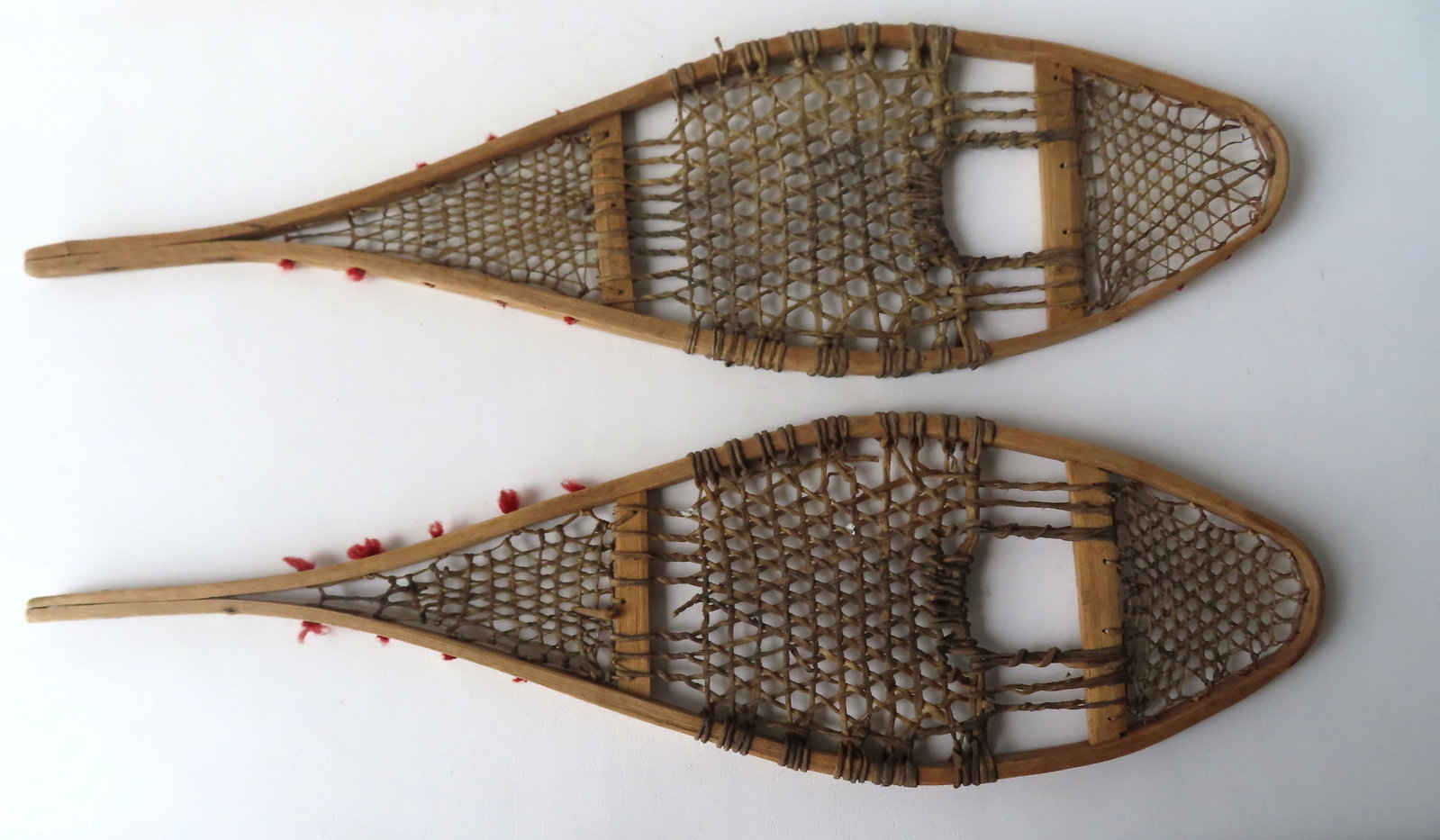 Pair of small Native American snow shoes, late 19th to early 20th century. Some losses to the: Pair of small Native American snow shoes, late 19th to early 20th century. Some losses to the attached red wool threads around border, else good condition. Measures 31"L x 9"W.