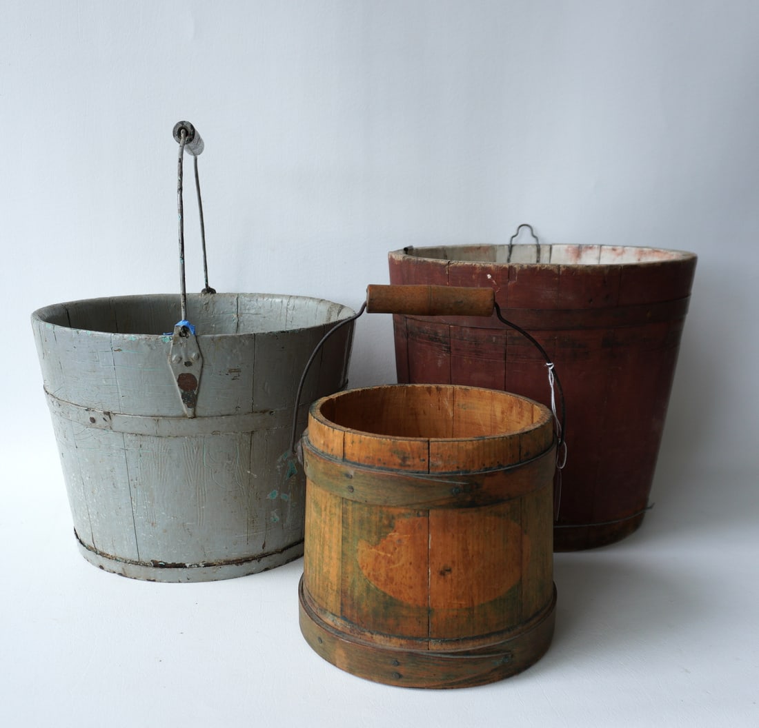Three primitive buckets, all 19th century including a sap bucket in original red paint (lower strap: Three primitive buckets, all 19th century including a sap bucket in original red paint (lower strap is broken and has been replaced by a modern wire to hold the staves together), a well bucket with ba