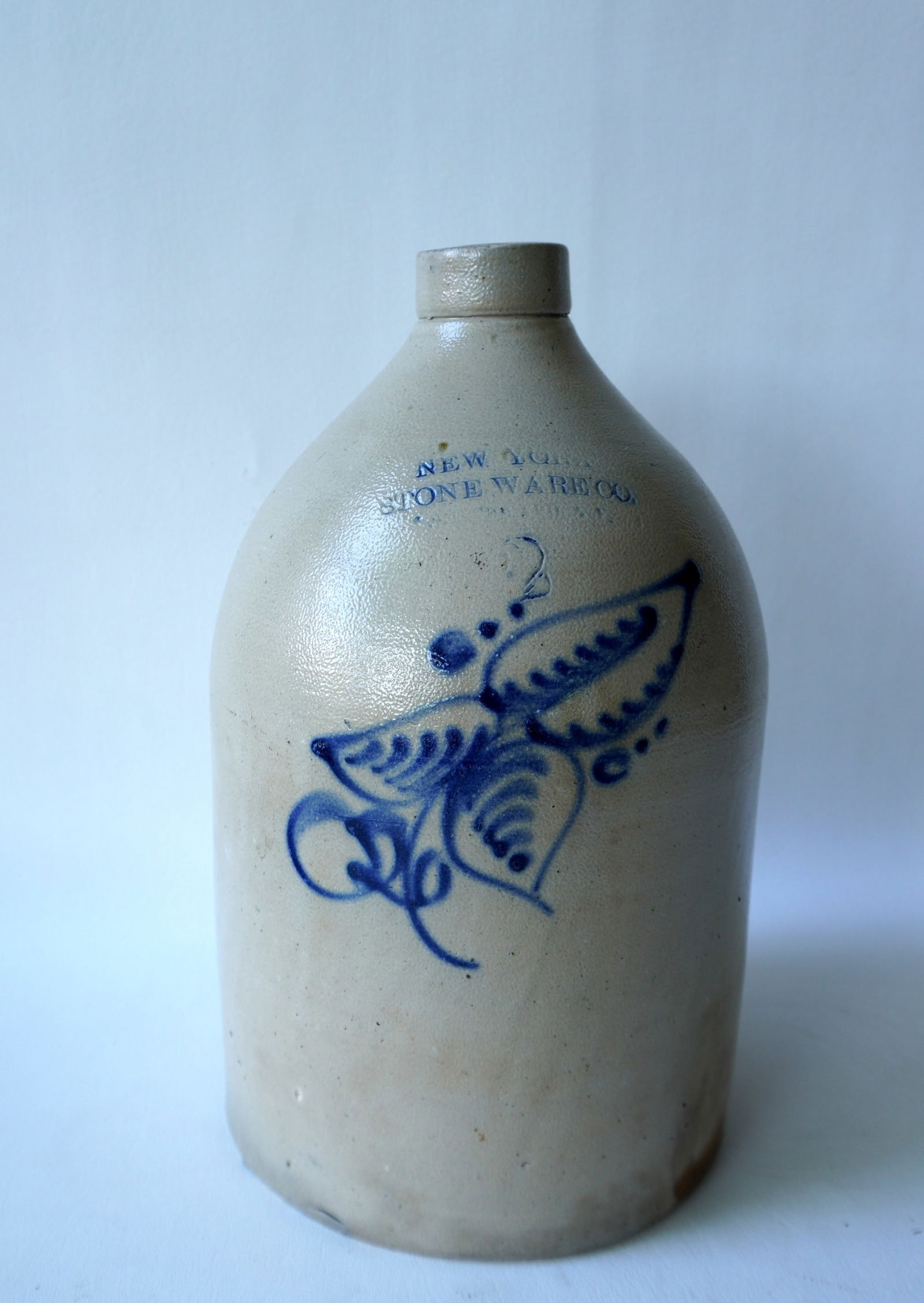 Stoneware jug, 2 gallon, decorated with a cobalt blue flower with the impressed mark of New York: Stoneware jug, 2 gallon, decorated with a cobalt blue flower with the impressed mark of New York Stoneware Co. Fort Edward NY. Slight separation in clay where handle meets the body, 2 small chips arou