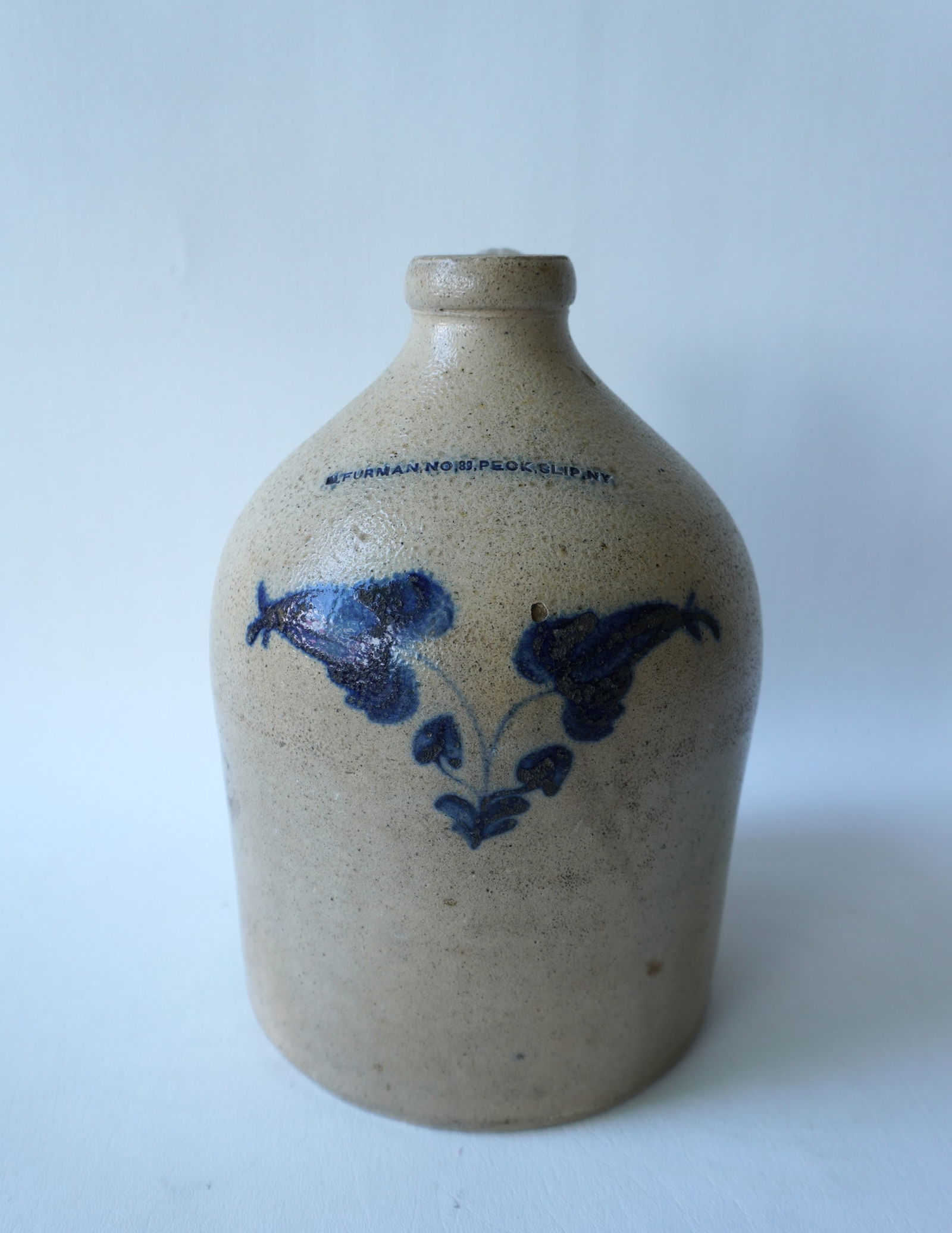 Stoneware jug, appears to be 1 gallon size, decorated with a cobalt blue double flower, with the: Stoneware jug, appears to be 1 gallon size, decorated with a cobalt blue double flower, with the impressed mark of M. Furman. No 89 Peck, Slip. NY. Slight glazing flake on interior of spout otherwise