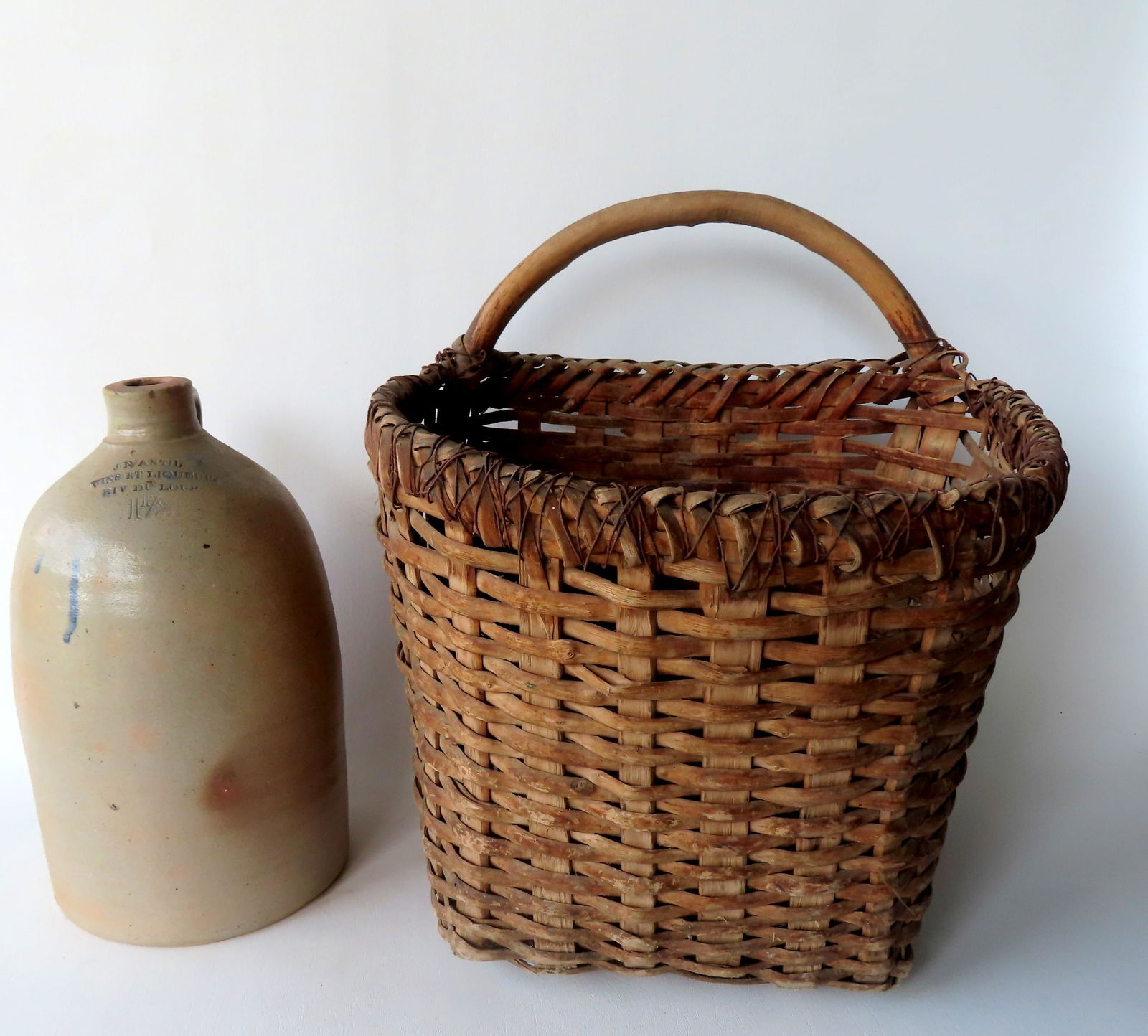 Two country items including: A Stoneware jug with the mark of a French wine and liquor store,: Two country items including: A Stoneware jug with the mark of a French wine and liquor store, probably Canadian late 19th century - 1 1/2" gallon - measures 14"H; and an unusual splint basket with sin