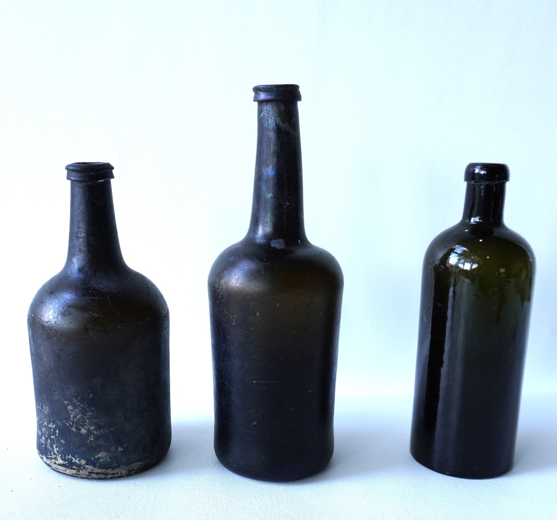 Three 19th century wine/spirits bottles including: Two iridescent sea bottles with pushed-up bottoms: Three 19th century wine/spirits bottles including: Two iridescent sea bottles with pushed-up bottoms and applied lips, the largest measuring 10 1/2"H x 3 1/2"W - both in very good condition; and an ol