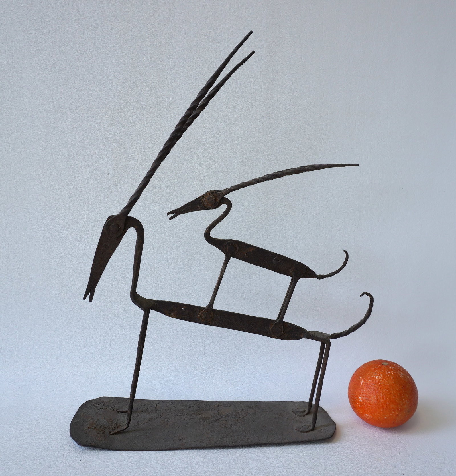 An Art Deco hand forged iron sculpture depicting a stylized baby antelope standing on the back of: An Art Deco hand forged iron sculpture depicting a stylized baby antelope standing on the back of another stylized antelope, mounted on tin base. The base with slight rust and bent on ends, otherwise 