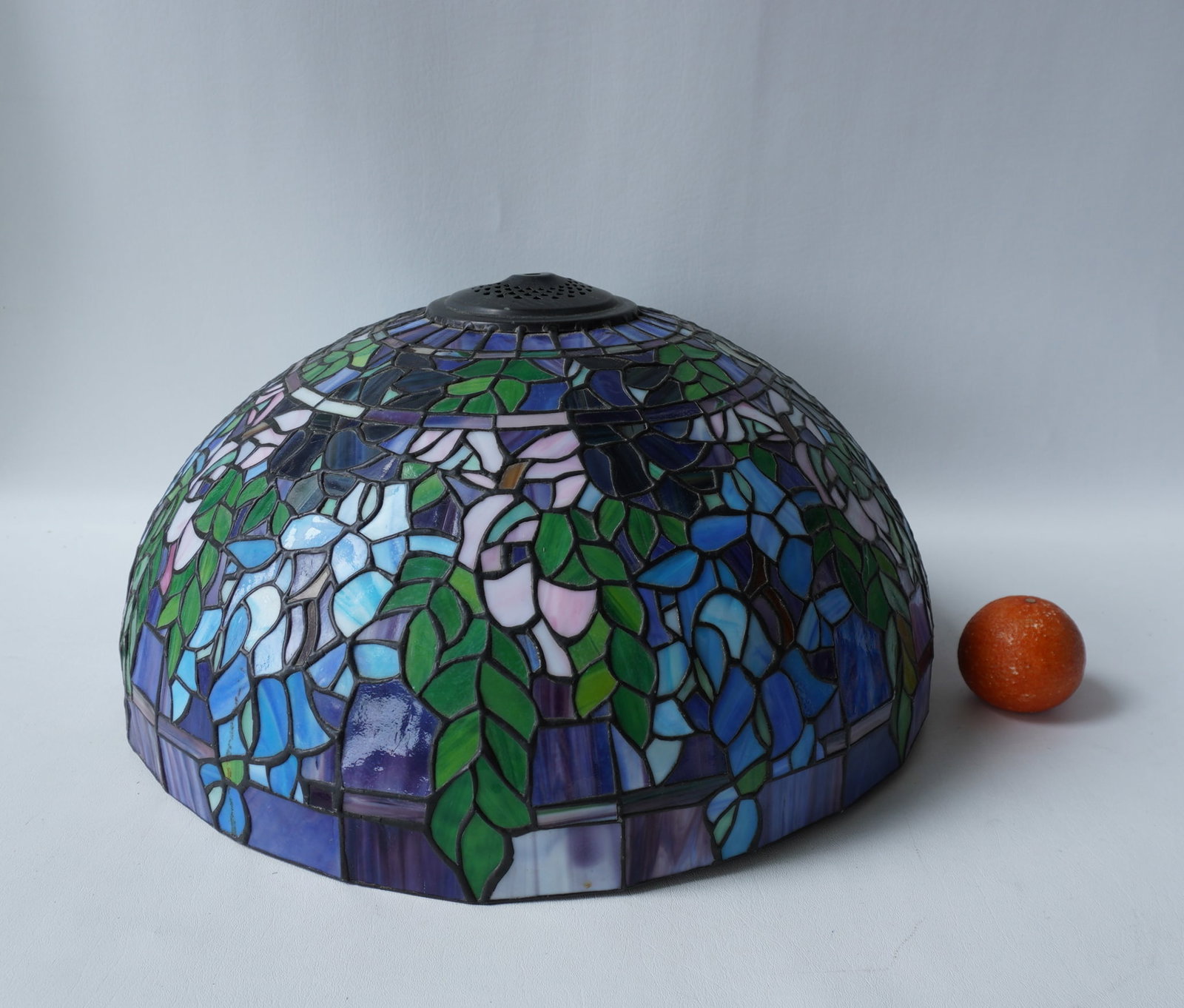 A colorful leaded and slag glass floral and leaf lamp shade in the Tiffany style, probably mid to: A colorful leaded and slag glass floral and leaf lamp shade in the Tiffany style, probably mid to late 20th century. Slight ding in the top central metal fitting, Otherwise very good condition - measu