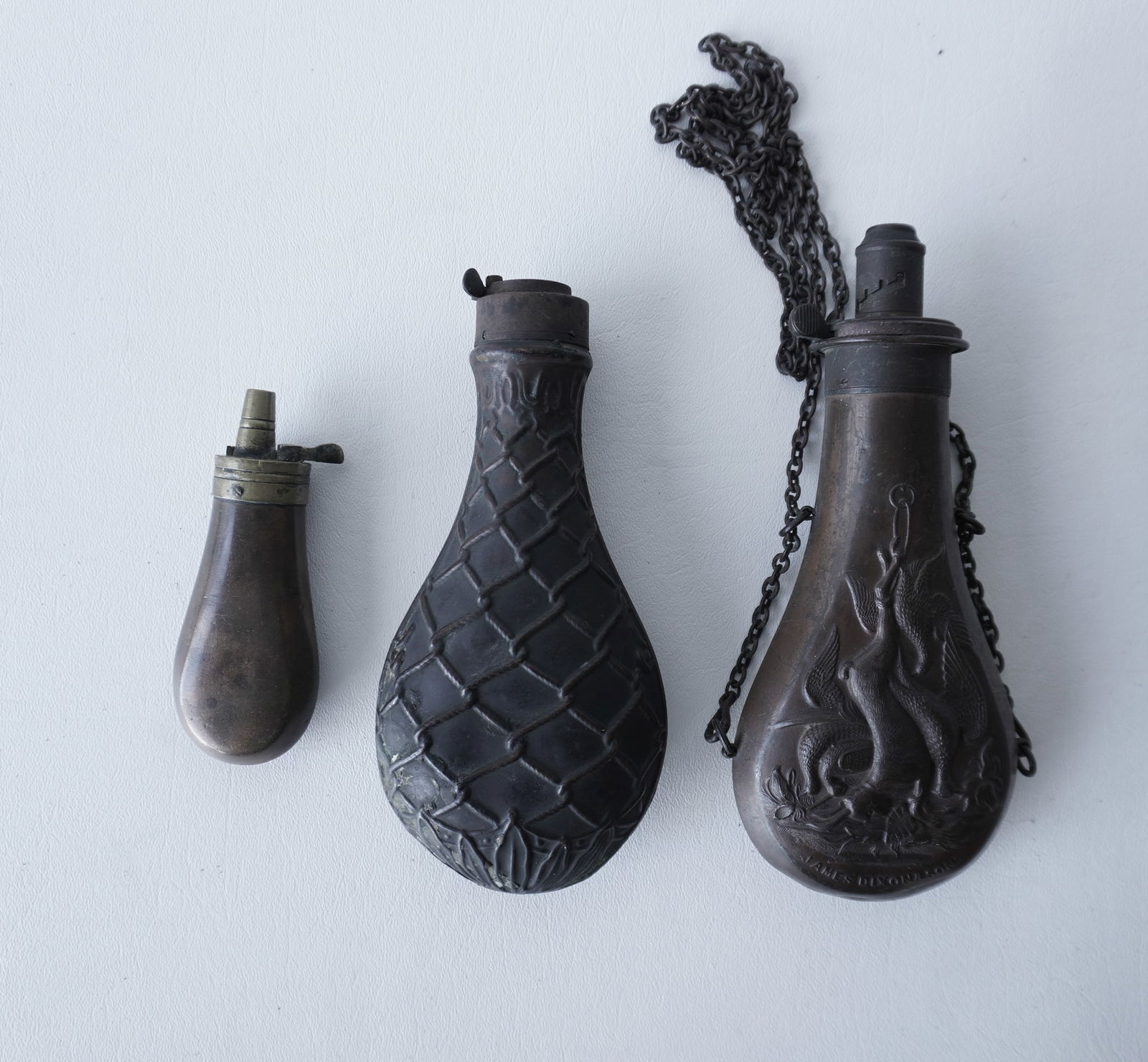 Three 19th century powder or shot flasks, including 1 in copper with embossed hanging game signed: Three 19th century powder or shot flasks, including 1 in copper with embossed hanging game signed James Dixon & Sons. All in good condition. The largest 7 3/4"L (retains some shot). Provenance: From t