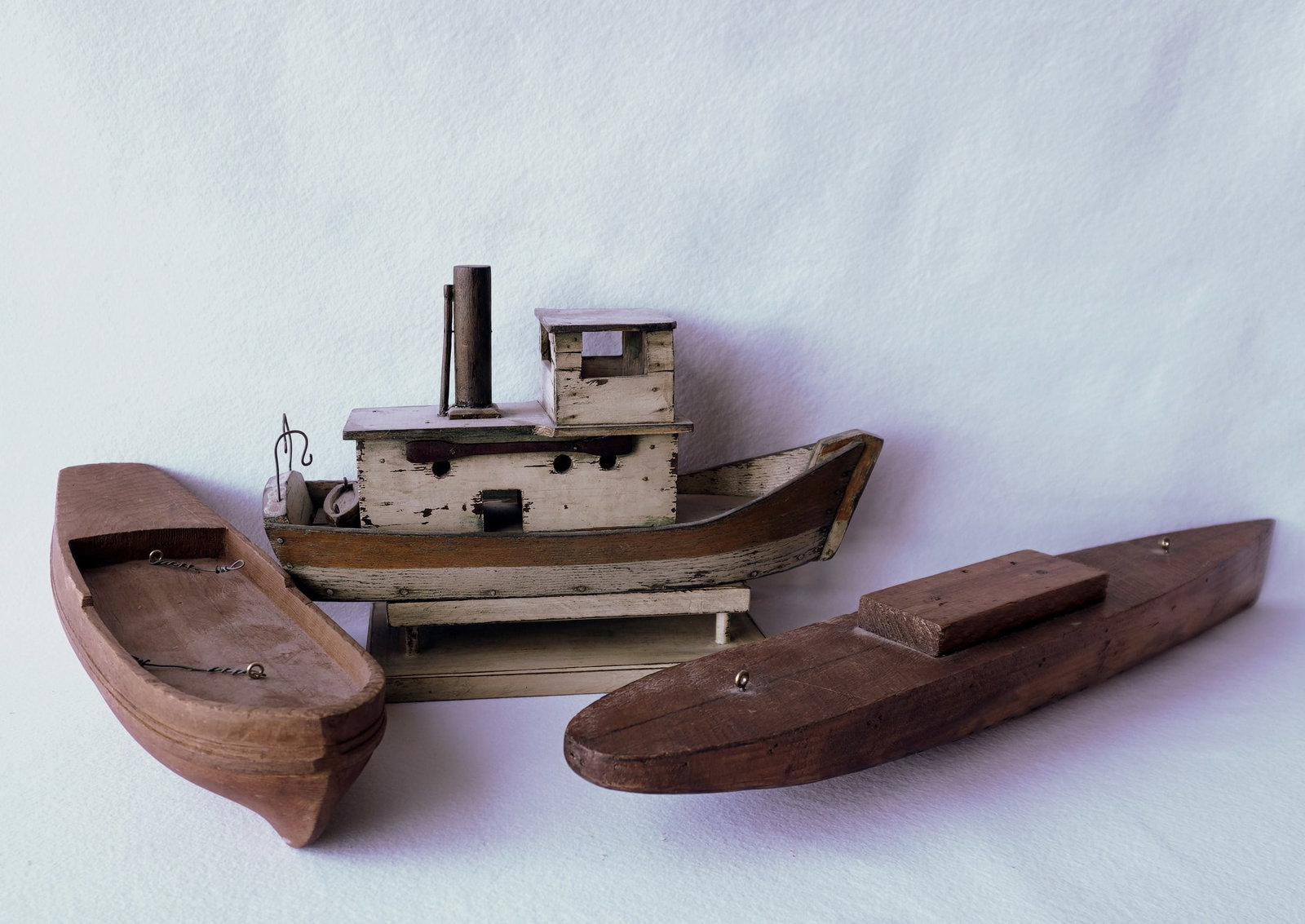 Three wooden handmade boat models including: A fishing boat with lifeboat in original paint, early: Three wooden handmade boat models including: A fishing boat with lifeboat in original paint, early to mid 20th century; and 2 full carved wooden hulls, early to mid 20th century. All in good condition