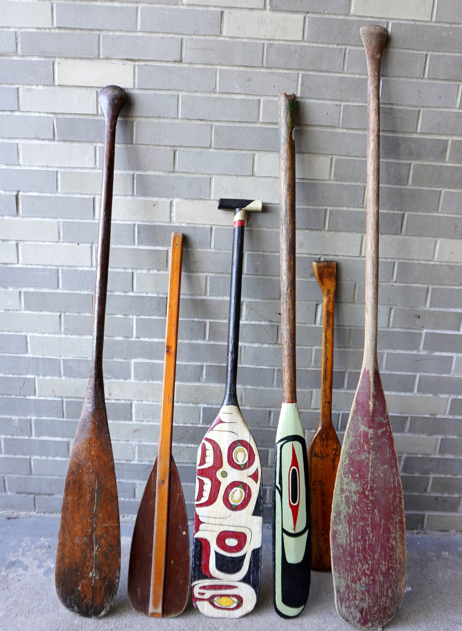 Grouping of 6 vintage boat paddles including 5 canoe and 1 rowboat with broken handle. The rowboat: Grouping of 6 vintage boat paddles including 5 canoe and 1 rowboat with broken handle. The rowboat paddle has been repainted in the Northwest coast design by Jeff Raymond and signed and dated "Raymond