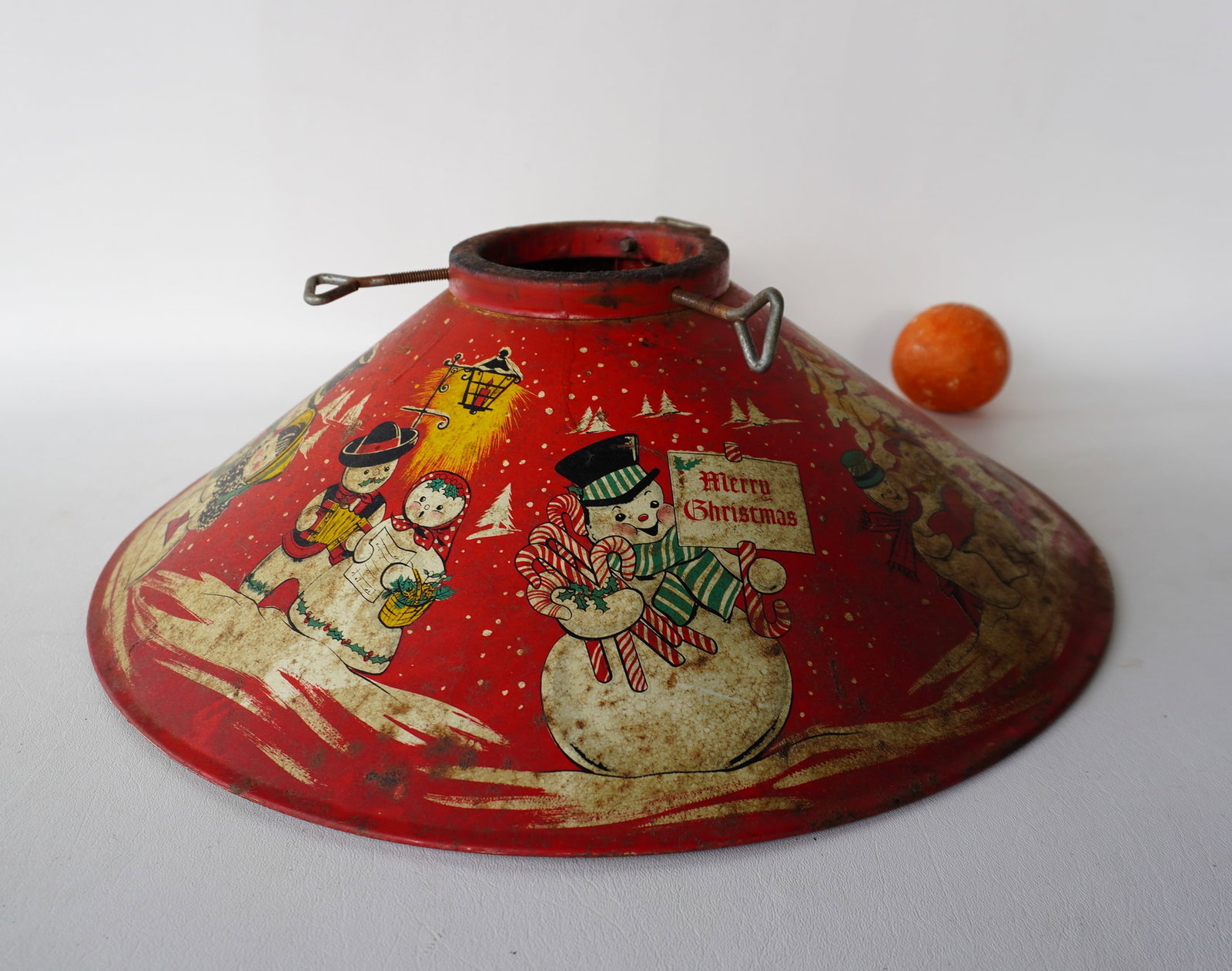 A lithographed tin Christmas tree stand decorated with snow men and women, circa 1950. Some surface: A lithographed tin Christmas tree stand decorated with snow men and women, circa 1950. Some surface rust - needs cleaning and overall fair to good condition. Measures 19 3/4" diameter x 5 3/4"H.
