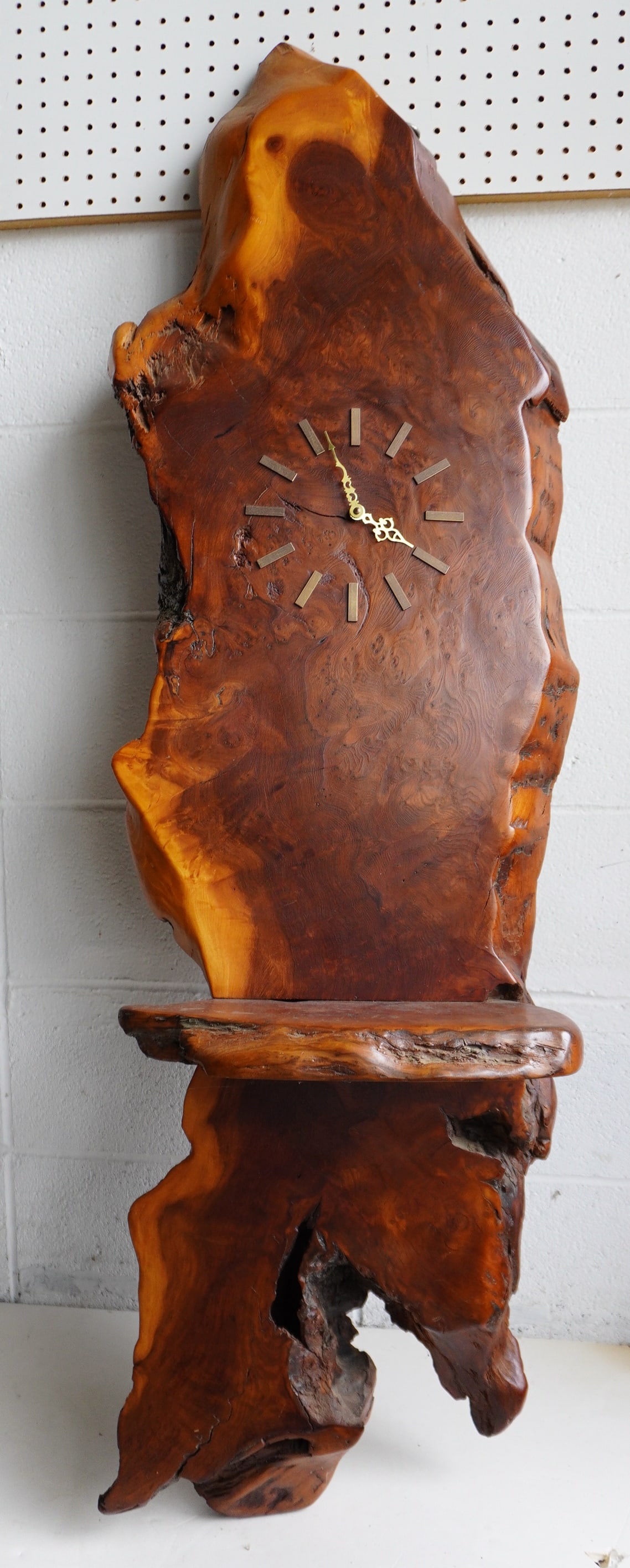 A large modern polished burlwood wall clock, with built in shelf, battery operated, reportedly from: A large modern polished burlwood wall clock, with built in shelf, battery operated, reportedly from Woodstock NY, circa 1970. Measures 57"H x 17"W x 8" thick. Clock has not been tested, but the burlwo