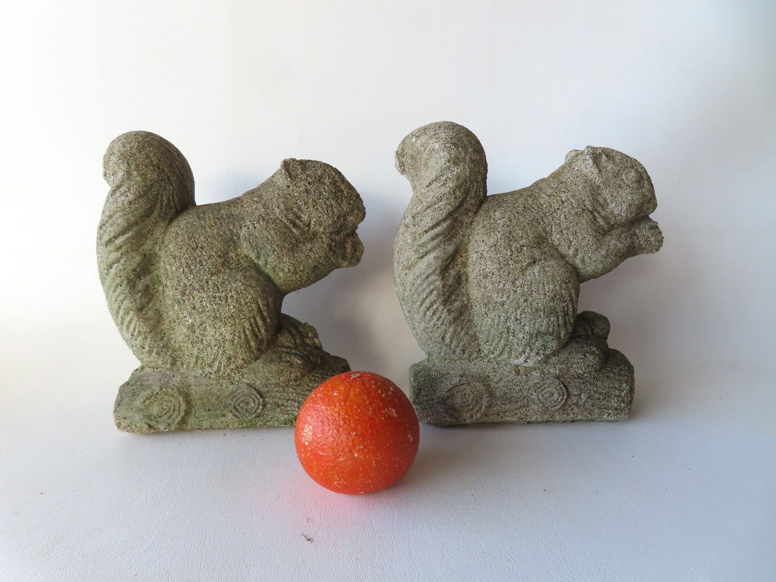 Two life size concrete squirrel ornaments for the garden, each eating nuts perched on logs, mid 20th