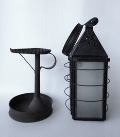Two early tin lighting devices. The first, a candle lantern with glass sides and pierced roof with