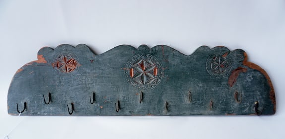 A carved wooden hanging game rack in old green paint over a salmon stain, having 11 hand forged iron