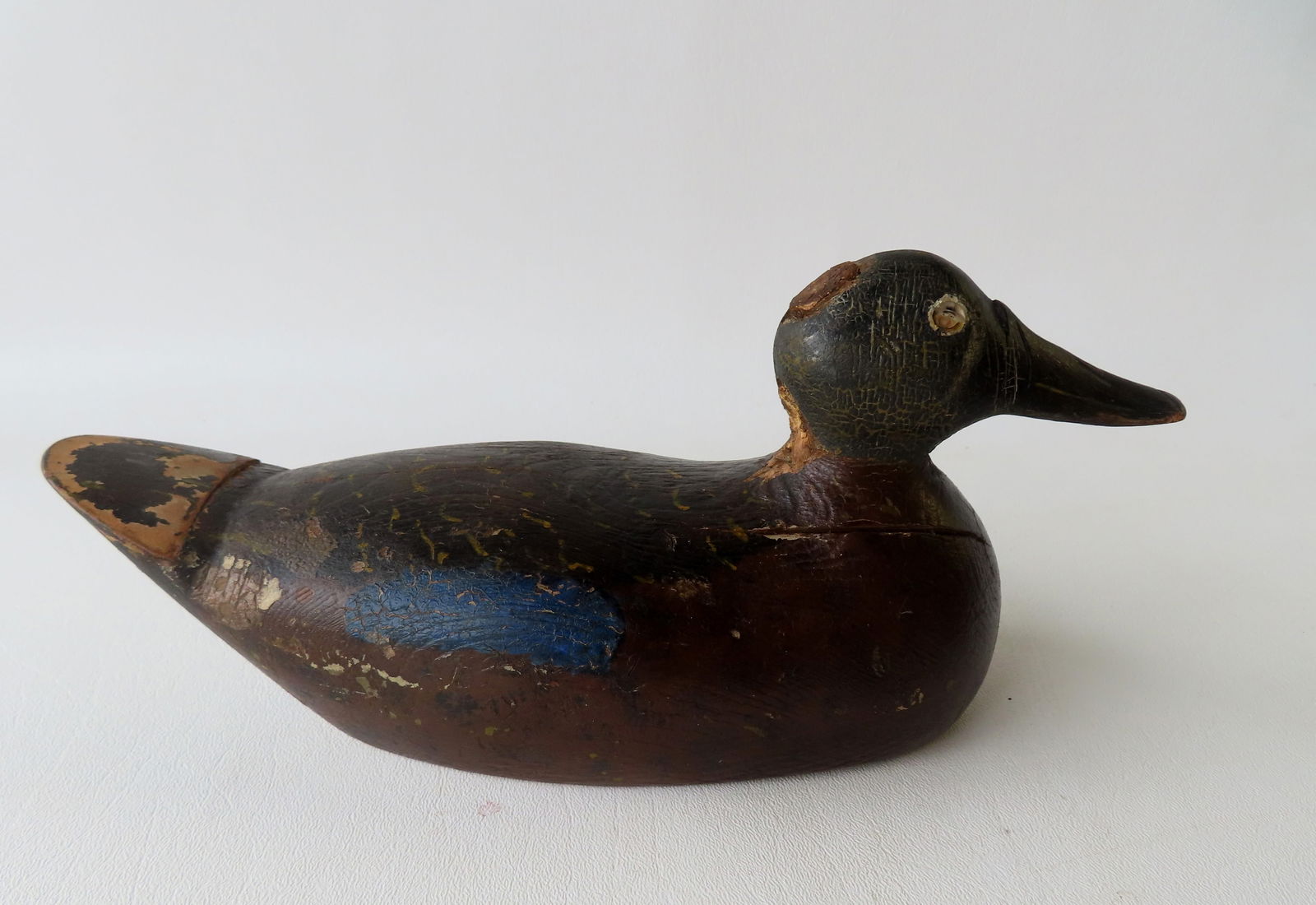 A folk art carved wooden decoy, 3/4 size, crusty old paint with carved beak and inset lead weight on: A folk art carved wooden decoy, 3/4 size, crusty old paint with carved beak and inset lead weight on base - missing one glass eye, extensive paint crazing, but overall good condition - 10 3/4" x 4 3/4