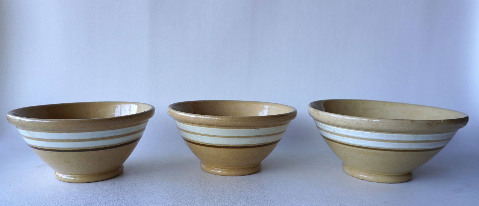 Three near matching yellowware mixing bowls in graduated sizes, each with rolled rims, white bands (1 of 13)