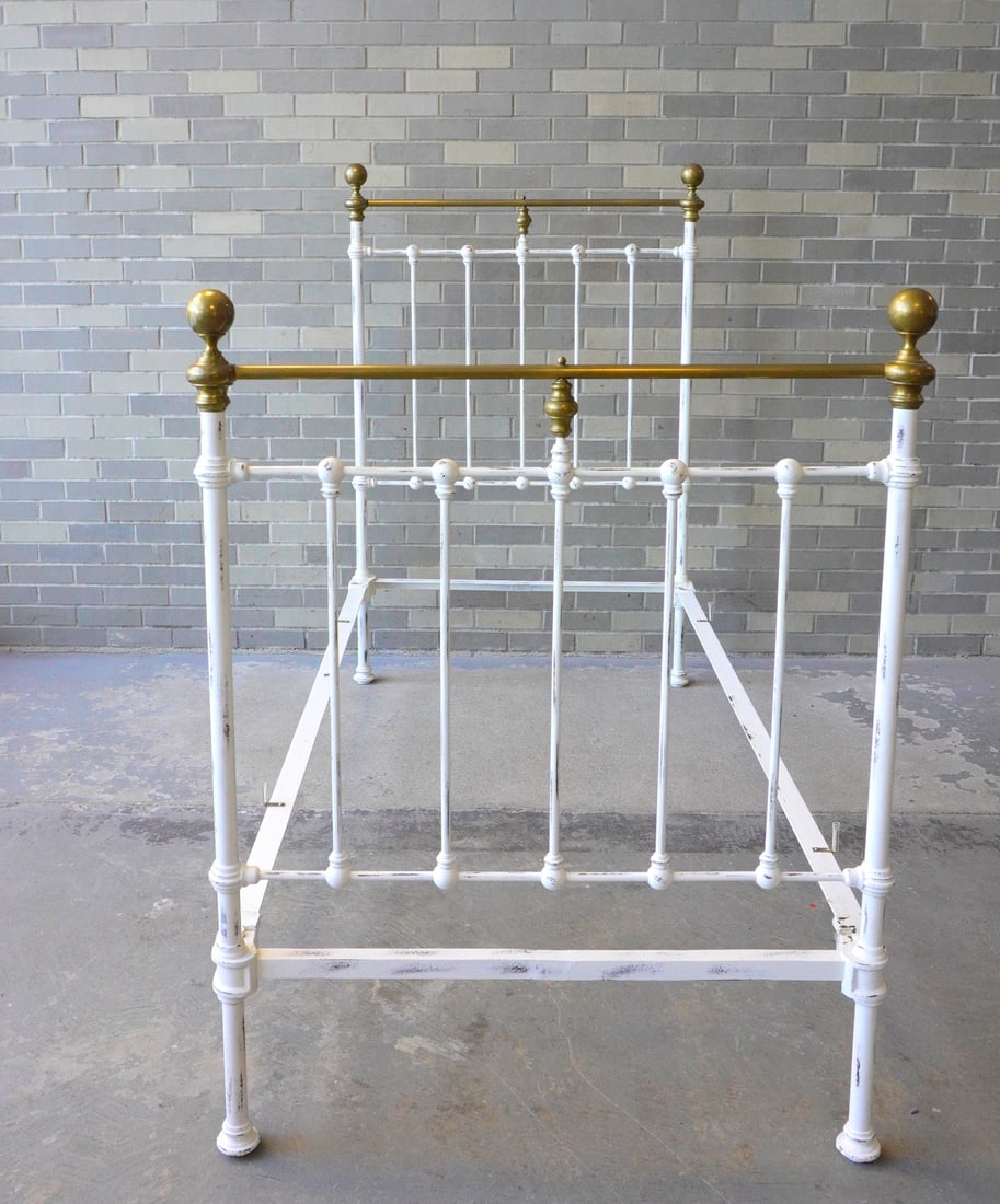 A 19th century brass and iron bed in white paint and with original side rails. The brass finials: A 19th century brass and iron bed in white paint and with original side rails. The brass finials with several dents, otherwise good condition (see photos). The overall size of bed measures 59"H x 39"W