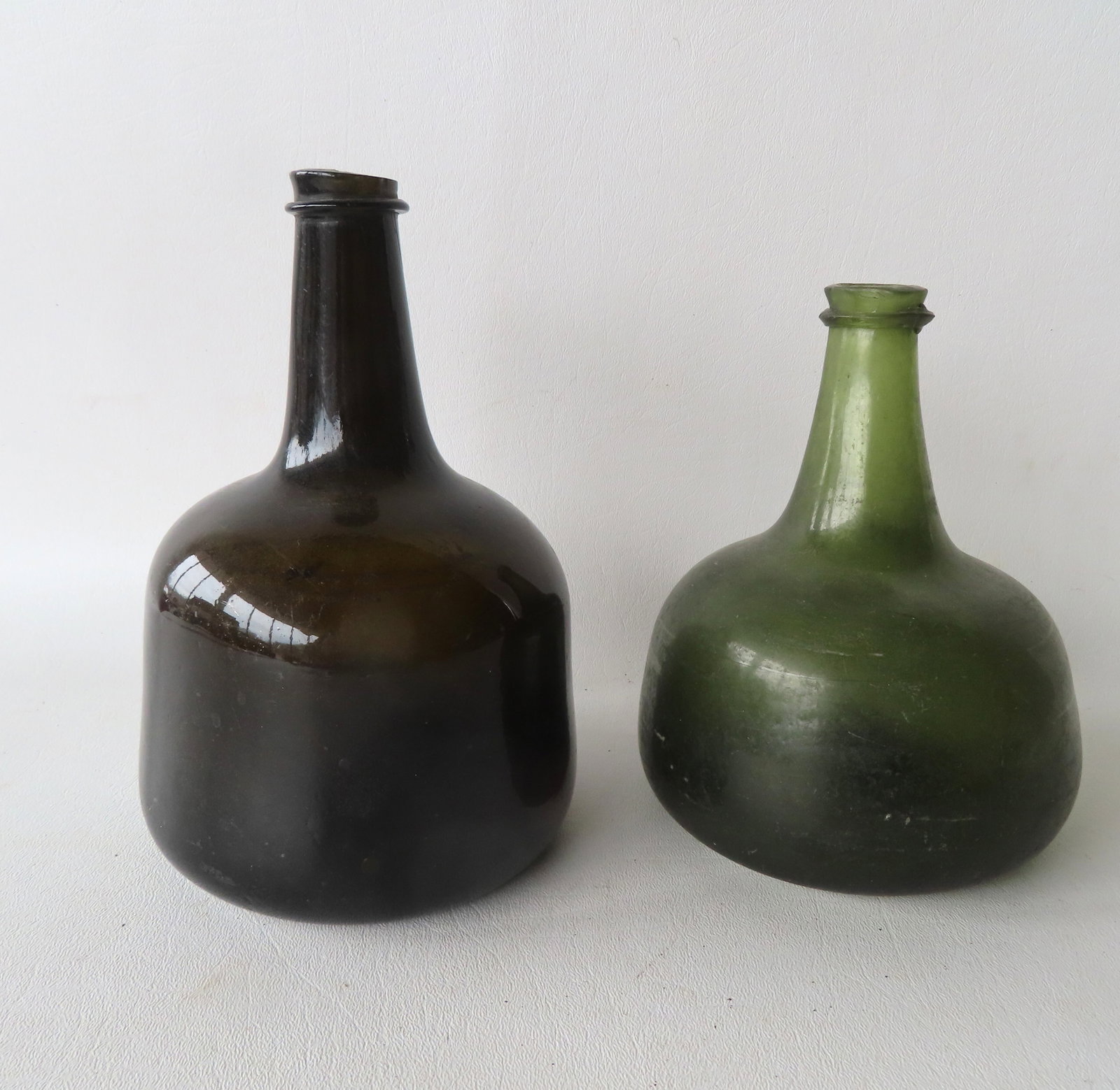 Two 18th/19th century squat wine bottles.: Two 18th/19th century squat wine bottles, all with kicked up bottoms and applied lips. One in light green - 2 tiny chips along edge of rim else very good condition; and the other in dark olive green -