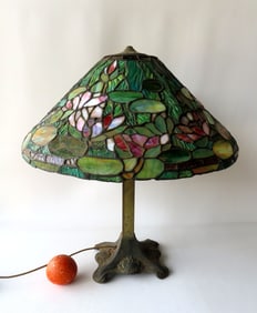 A slag glass table lamp mounted on an Arts & Crafts period base with brass column. The lamp itself