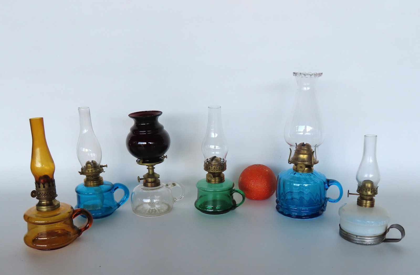 Grouping of 6 miniature oil lamps, all with finger holders - the white opalescent lamp is marked: Grouping of 6 miniature oil lamps, all with finger holders - the white opalescent lamp is marked "Manilla / Pat. Applied For" and is mounted within a separate tin holder from the same period. The colo