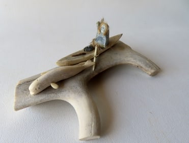 A hand painted carved bone sculpture depicting an Eskimo in Kayak holding spear