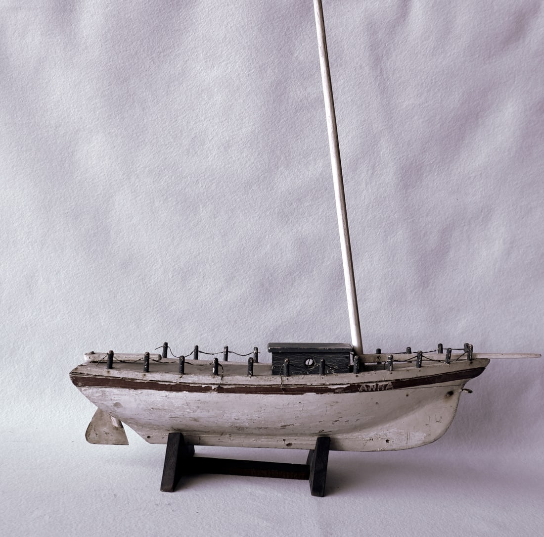 A handmade sailboat model with operational rudder and in old paint, early 20th century. Missing: A handmade sailboat model with operational rudder and in old paint, early 20th century. Missing sails and a small piece along the railing at the stern of boat, and several posts around perimeter, else