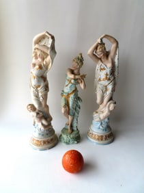Three porcelain figurines , 2 of semi-nude ladies with cherubs - one with several chips along the