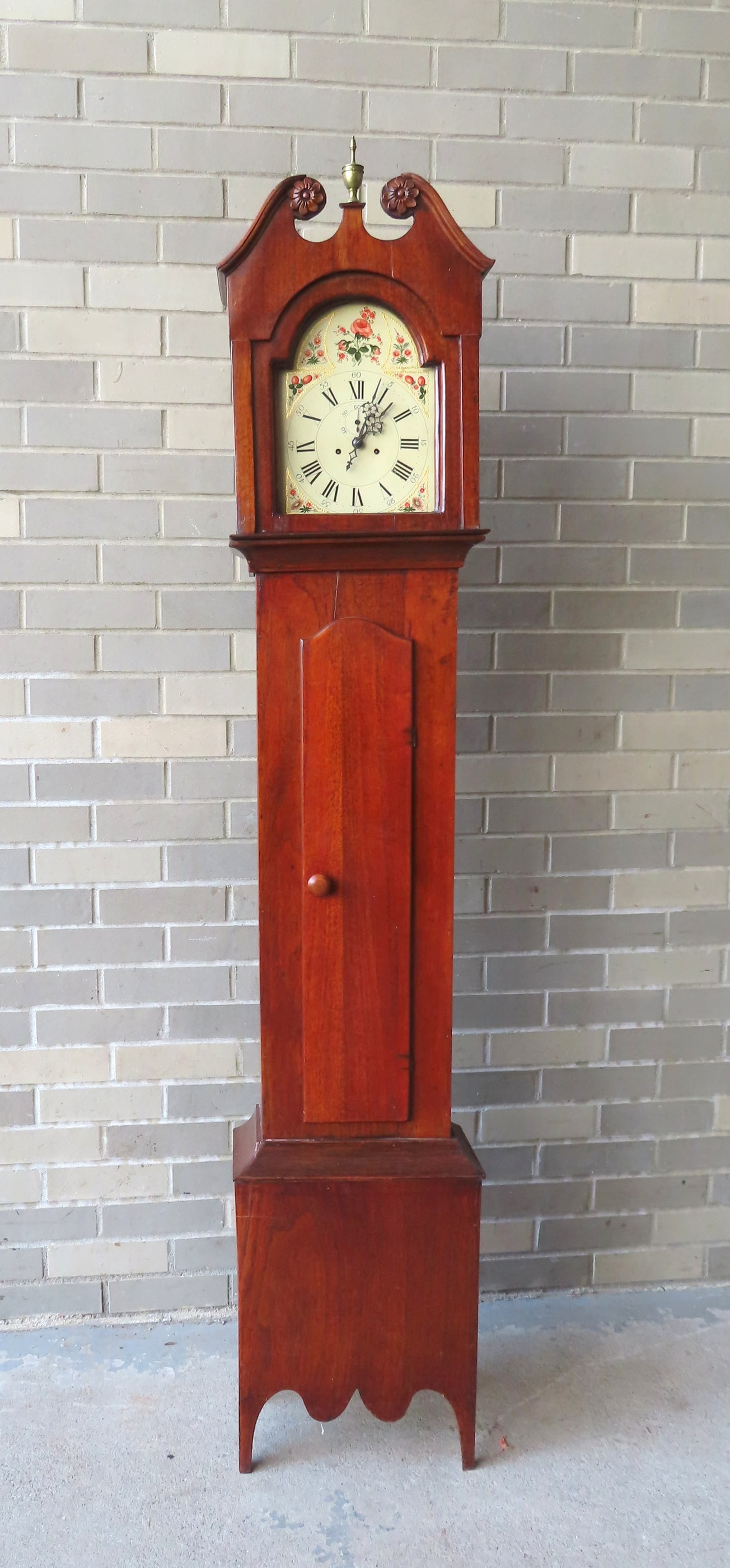 A mahogany Hepplewhite grandmother's clock, early 19th century. The clock case with broken arch top: A mahogany Hepplewhite grandmother's clock, early 19th century. The clock case with broken arch top with carved rosettes on terminals of arch, flanking a brass urn finial - beautiful cutout base. The 